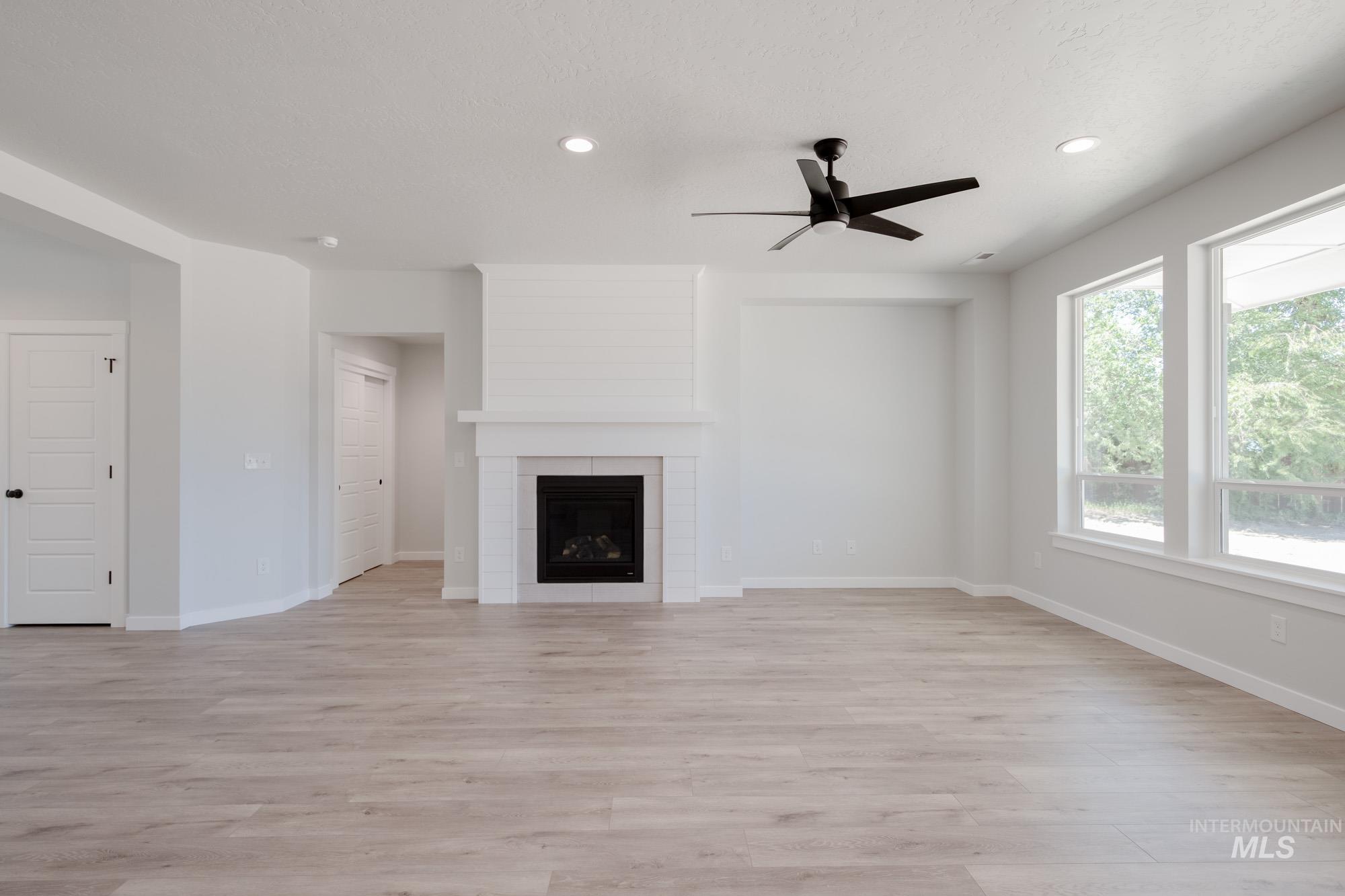 Unfurnished living room with a tiled fireplace, light wood finished floors, ceiling fan, and recessed lighting