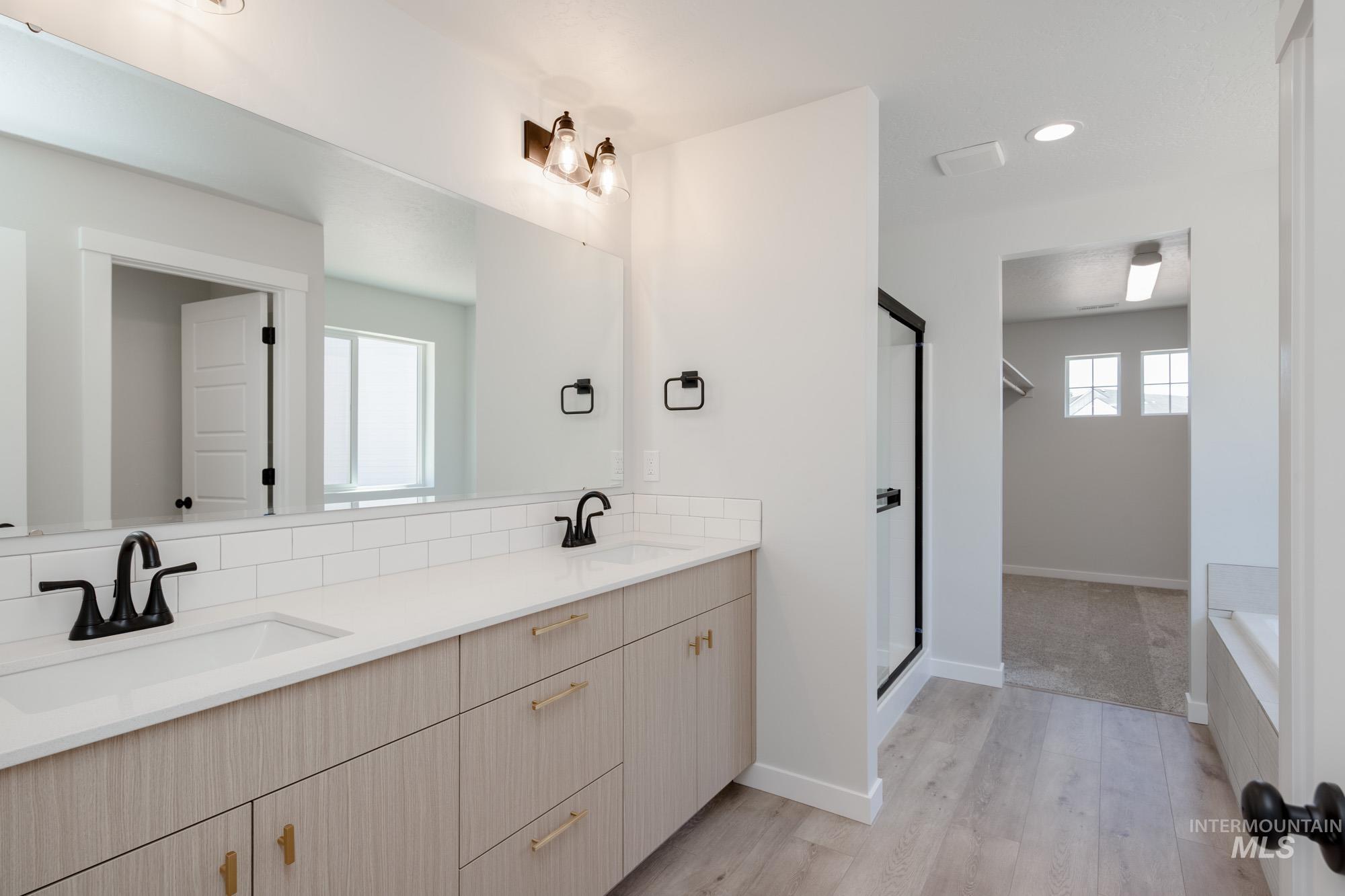 Bathroom with double vanity, light wood-style flooring, a stall shower, recessed lighting, and a bath