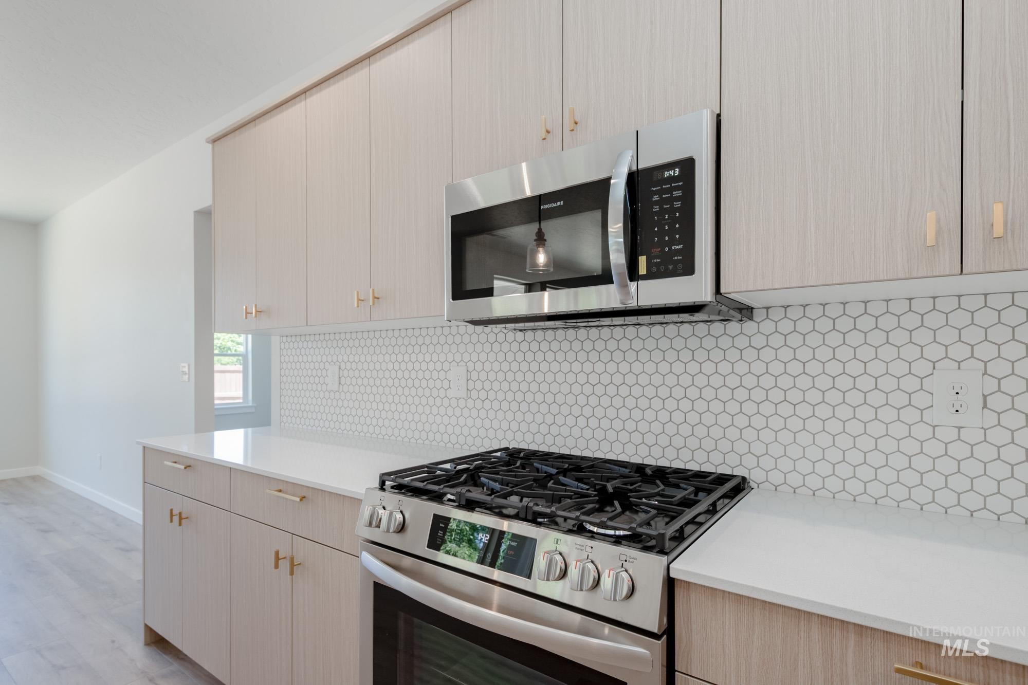 Kitchen with stainless steel appliances, tasteful backsplash, light brown cabinetry, light wood-style flooring, and modern cabinets