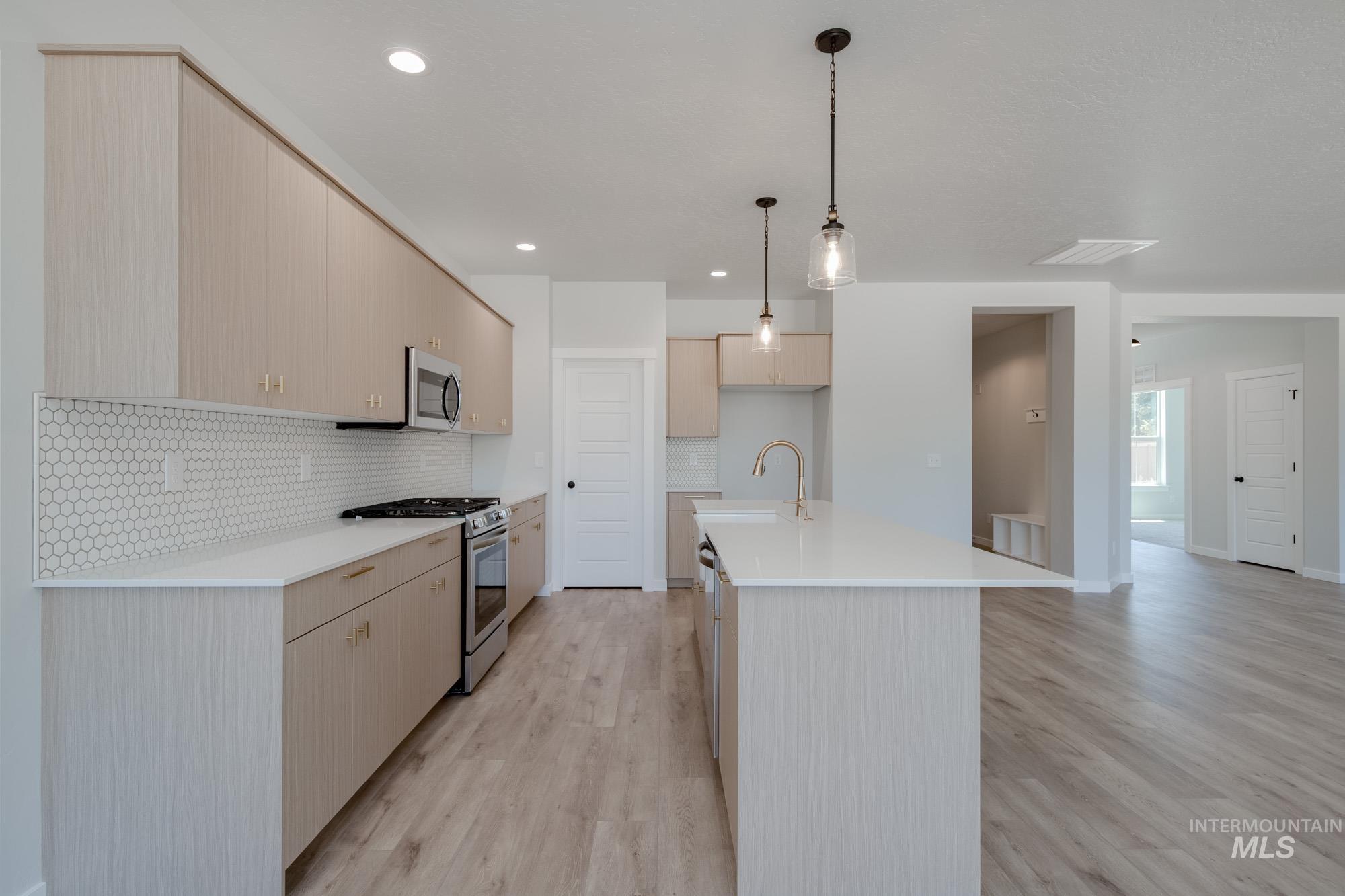 Kitchen featuring hanging light fixtures, appliances with stainless steel finishes, light wood-type flooring, a center island with sink, and recessed lighting