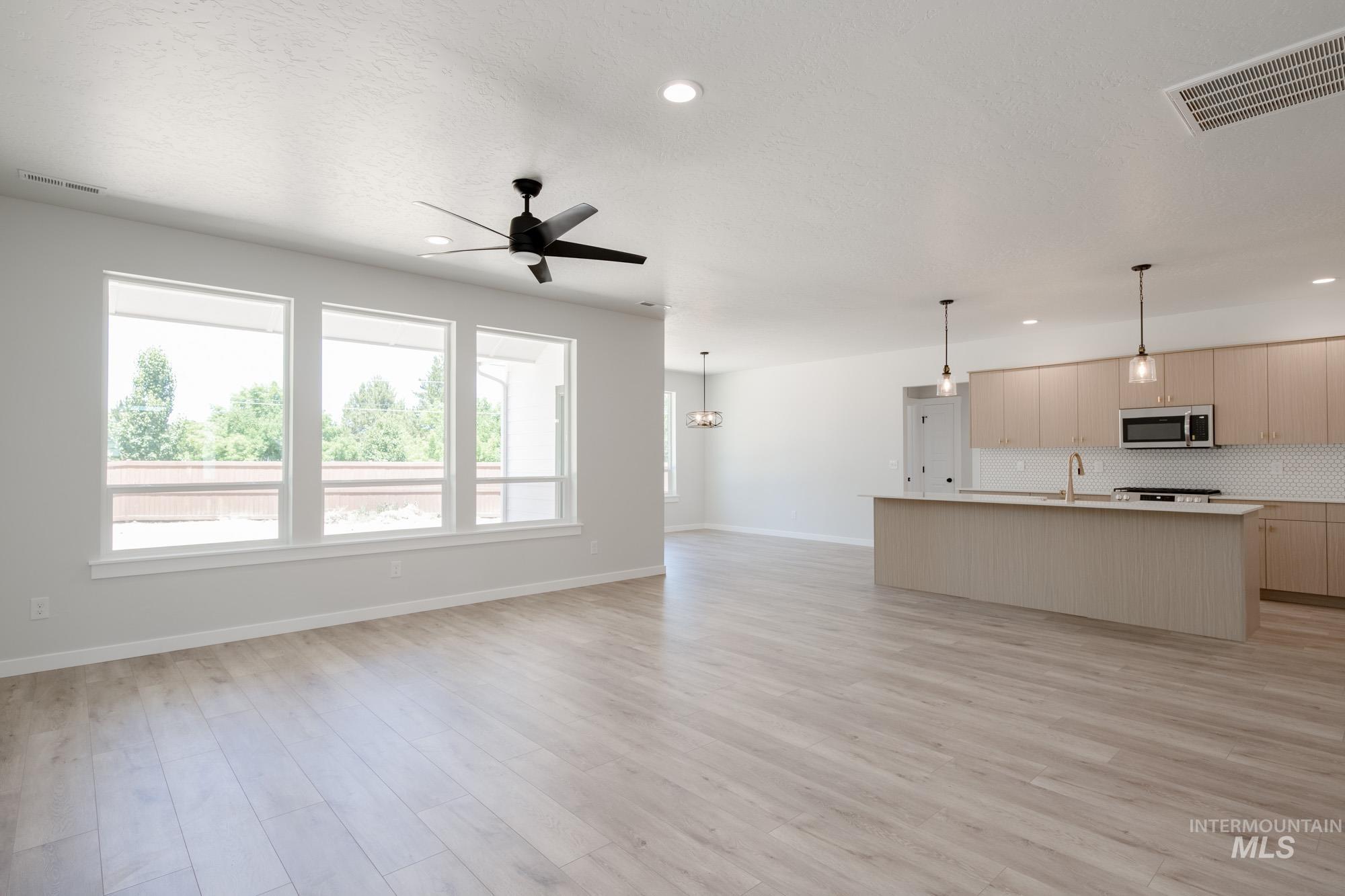 Unfurnished living room with a ceiling fan, light wood-style floors, recessed lighting, and a chandelier