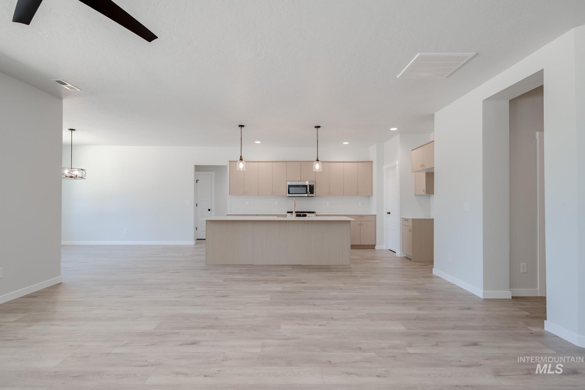 Kitchen with open floor plan, light countertops, an island with sink, decorative light fixtures, and backsplash