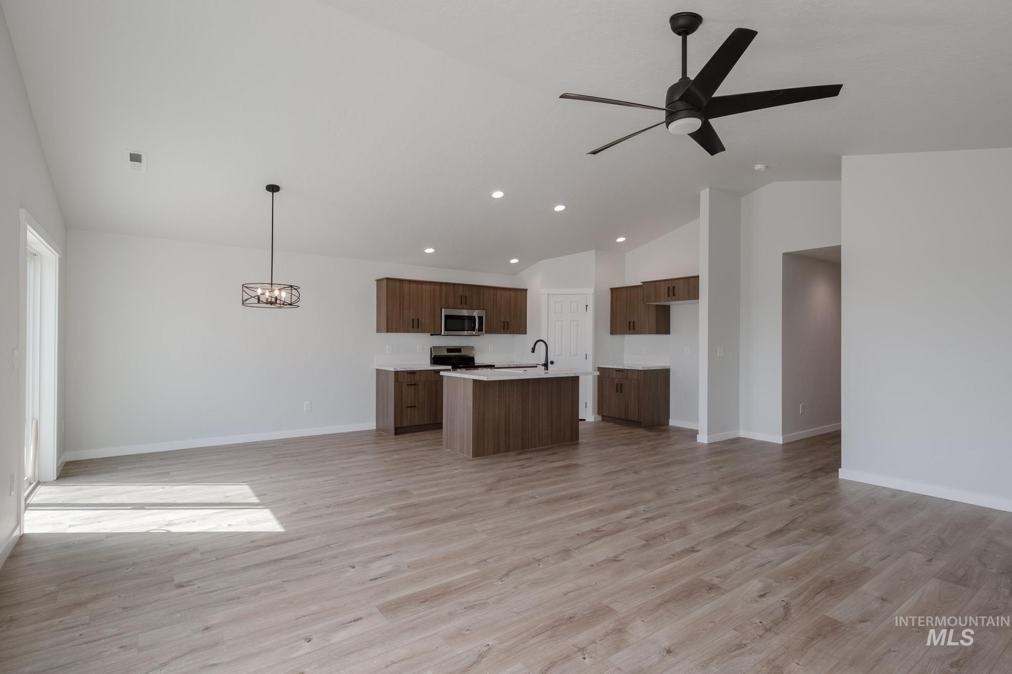 Kitchen featuring open floor plan, lofted ceiling, light countertops, a center island with sink, and light wood-type flooring