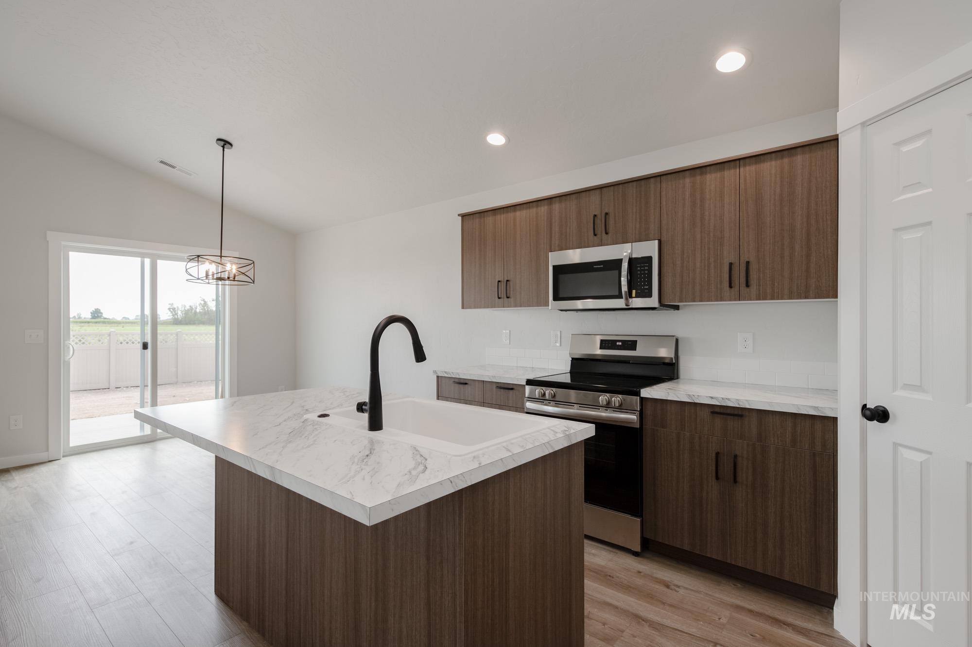 Kitchen featuring stainless steel appliances, light countertops, lofted ceiling, a kitchen island with sink, and light wood finished floors