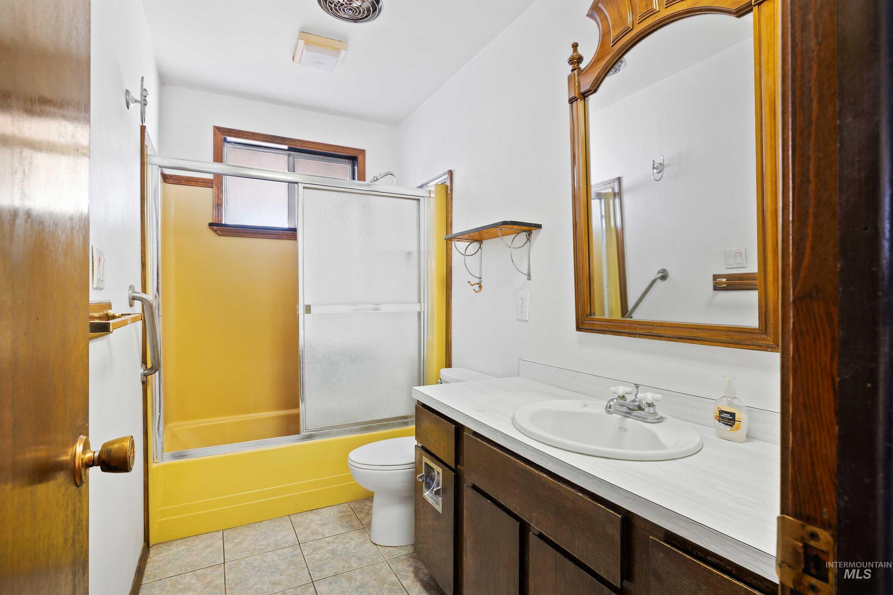 Full bath featuring combined bath / shower with glass door, vanity, and light tile patterned floors