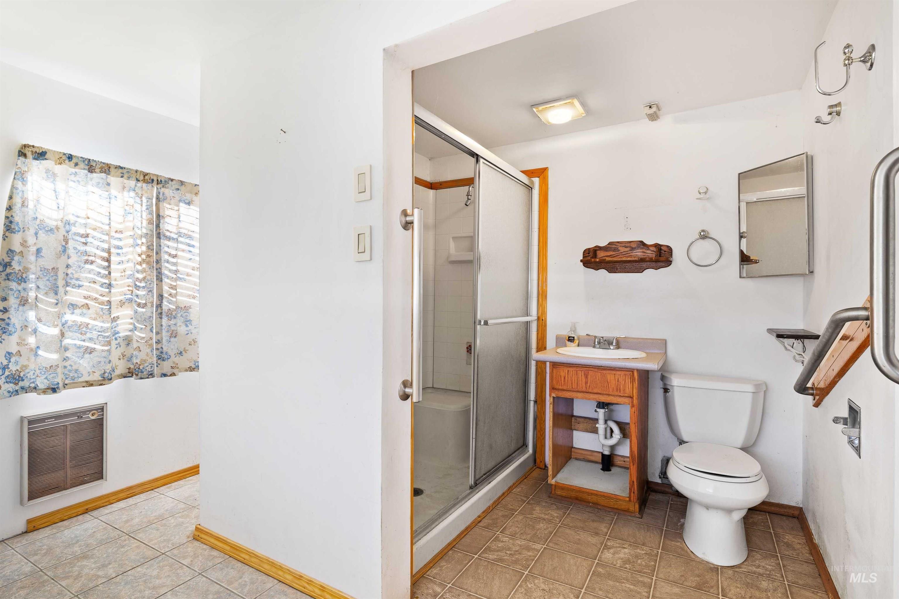Full bathroom with a stall shower, light tile patterned floors, heating unit, and vanity