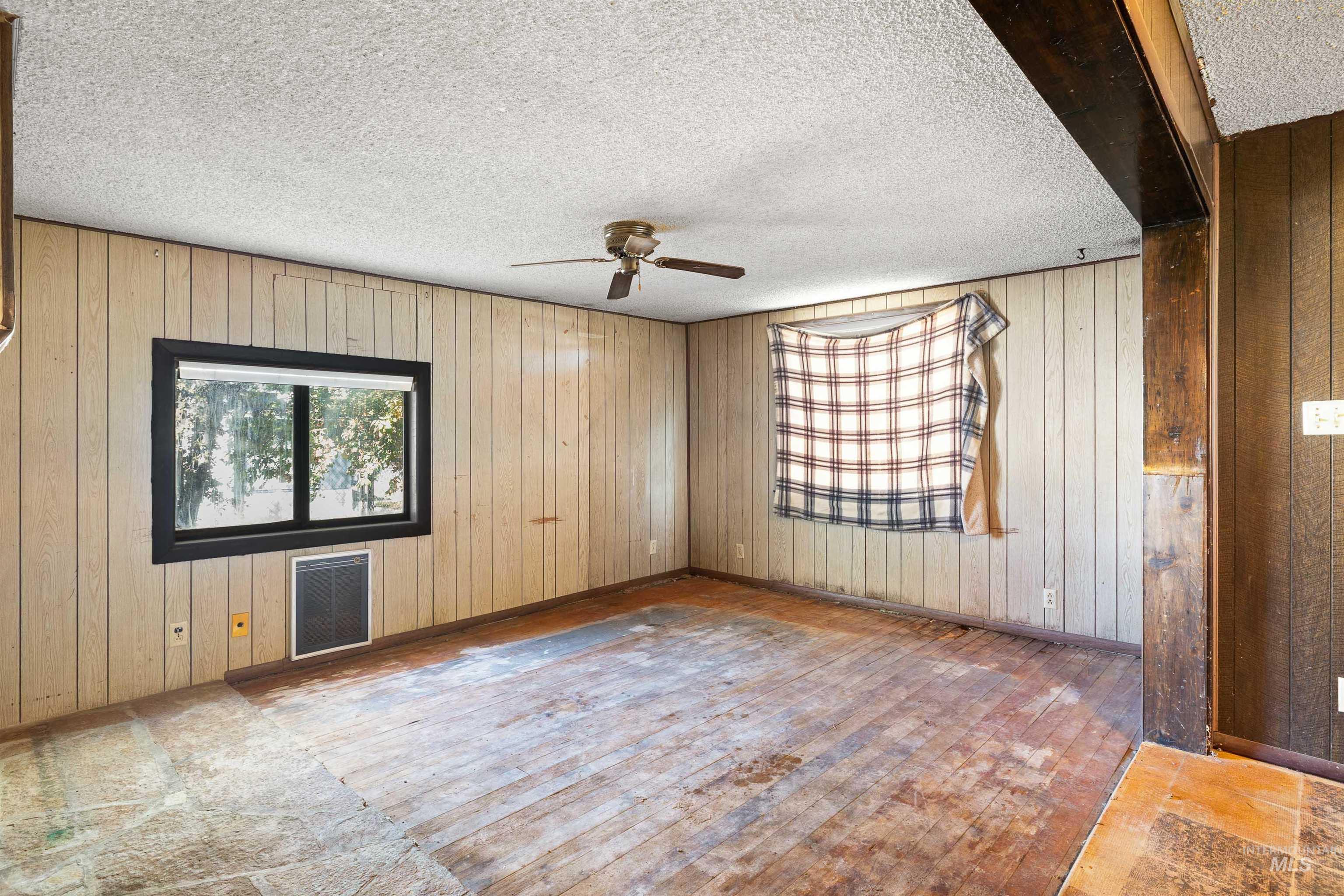 Unfurnished room featuring wood-type flooring, wooden walls, a textured ceiling, and a ceiling fan