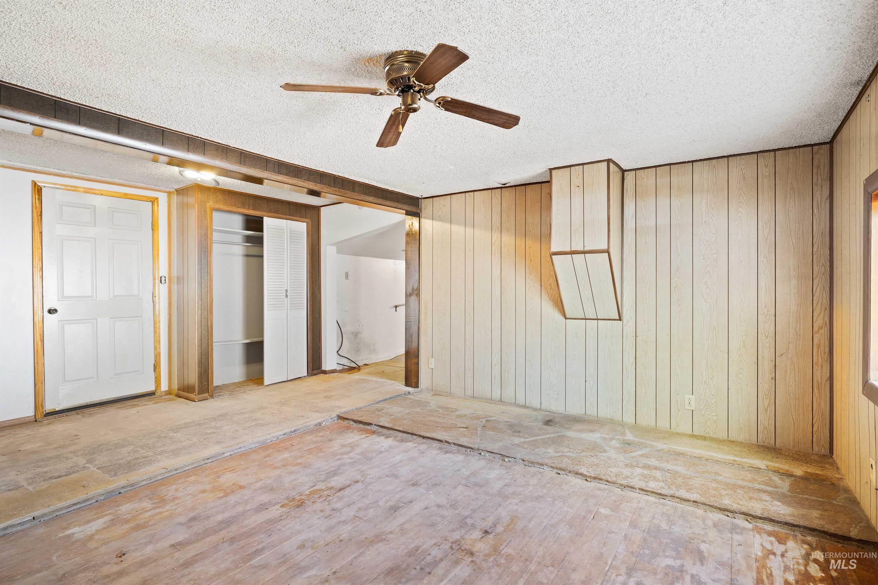 Unfurnished bedroom with a textured ceiling, a closet, a ceiling fan, and wooden walls