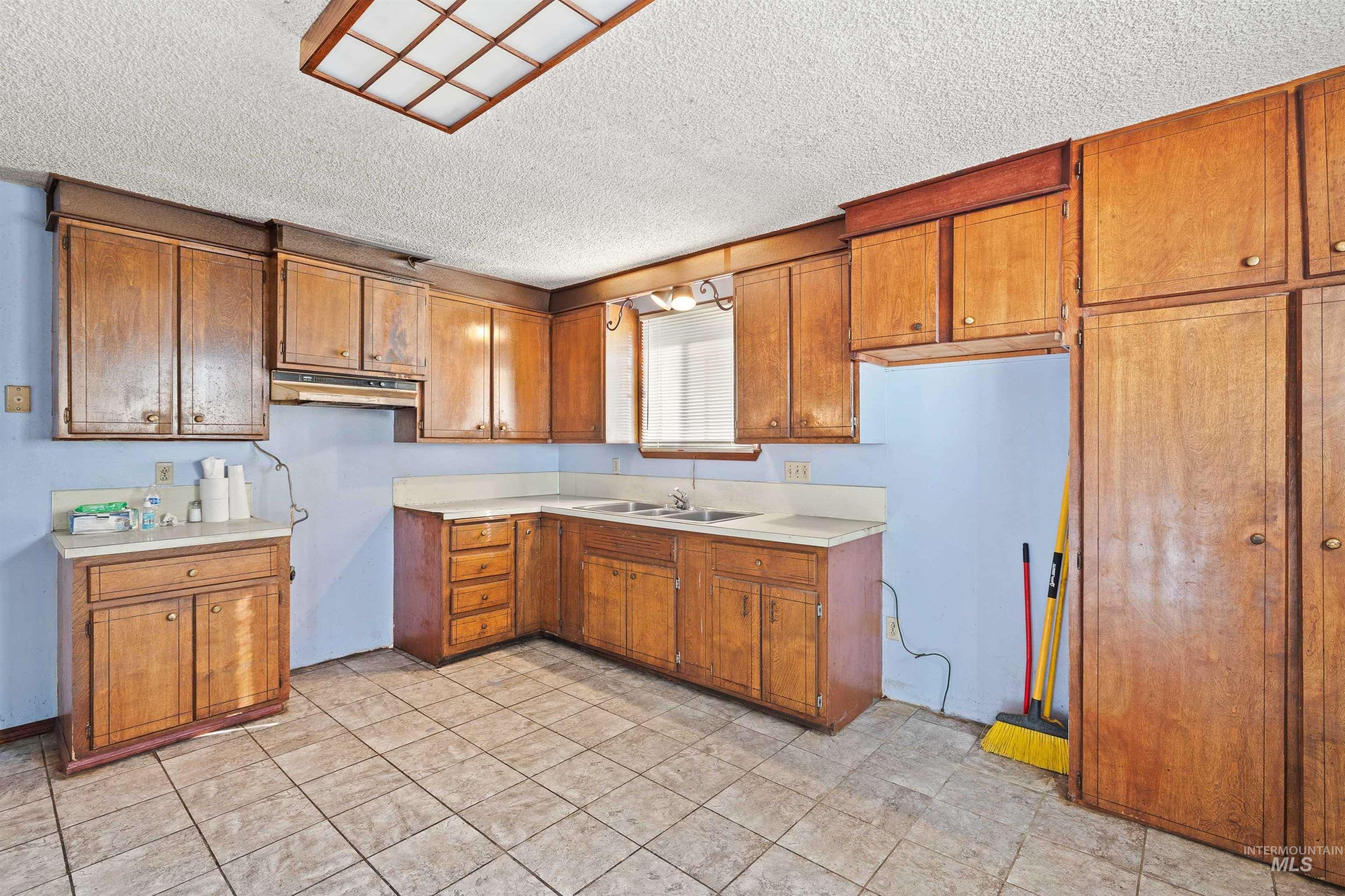 Kitchen featuring brown cabinets, light countertops, a textured ceiling, light tile patterned floors, and under cabinet range hood