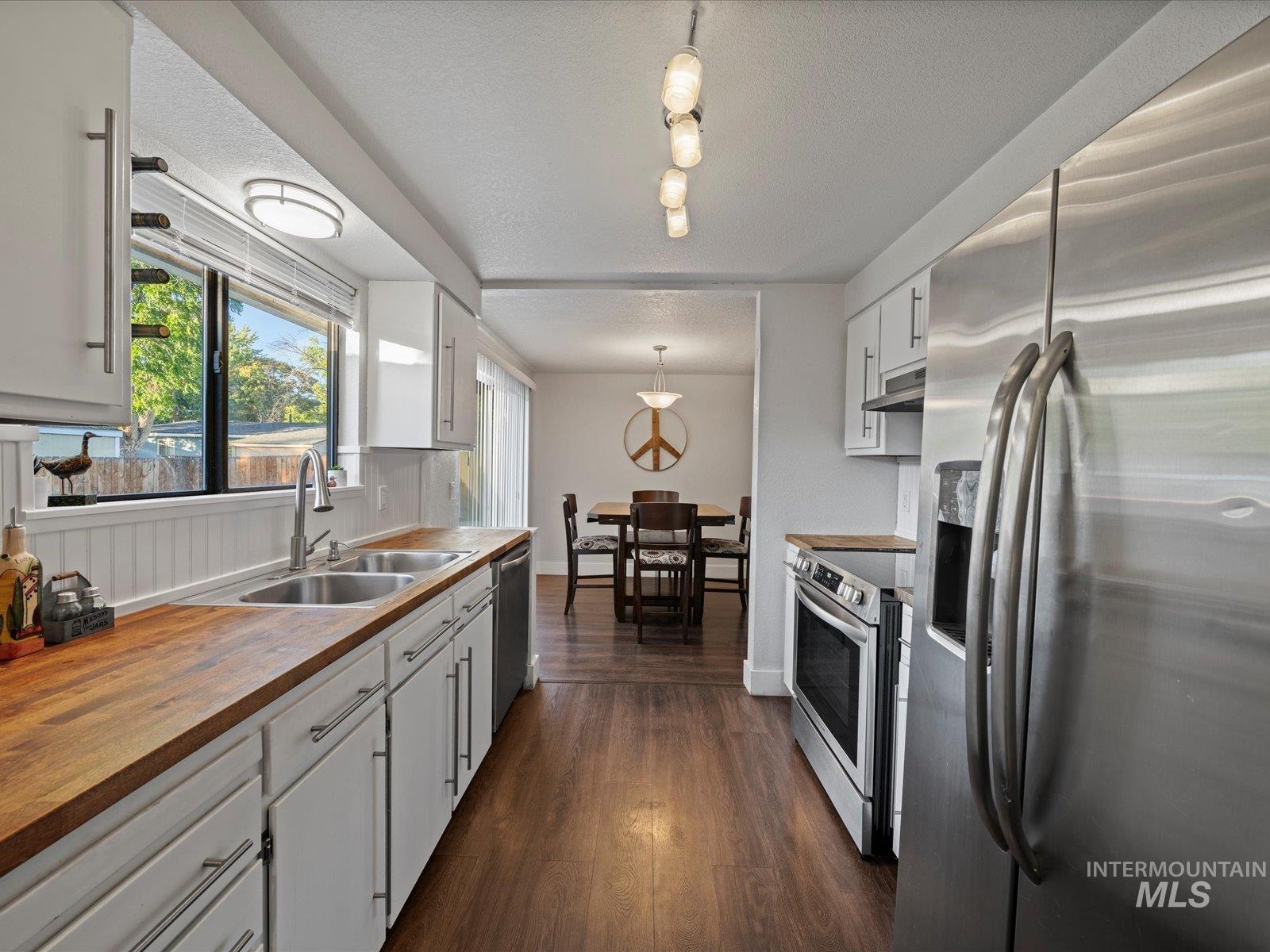 Kitchen featuring appliances with stainless steel finishes, white cabinetry, dark wood finished floors, pendant lighting, and butcher block countertops