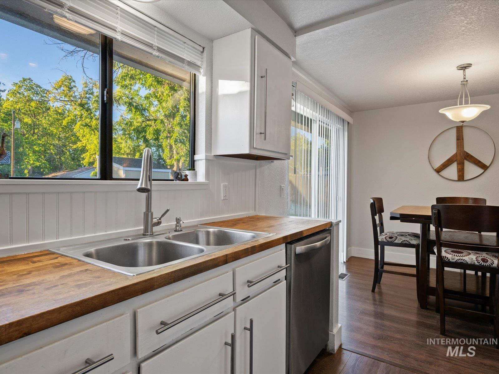 Kitchen with white cabinetry, butcher block countertops, dark wood-style flooring, stainless steel dishwasher, and pendant lighting