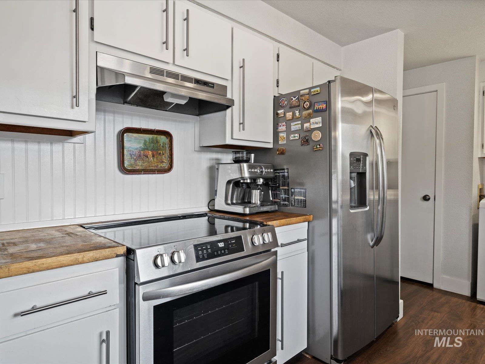 Kitchen with butcher block countertops, stainless steel appliances, under cabinet range hood, and dark wood-style floors