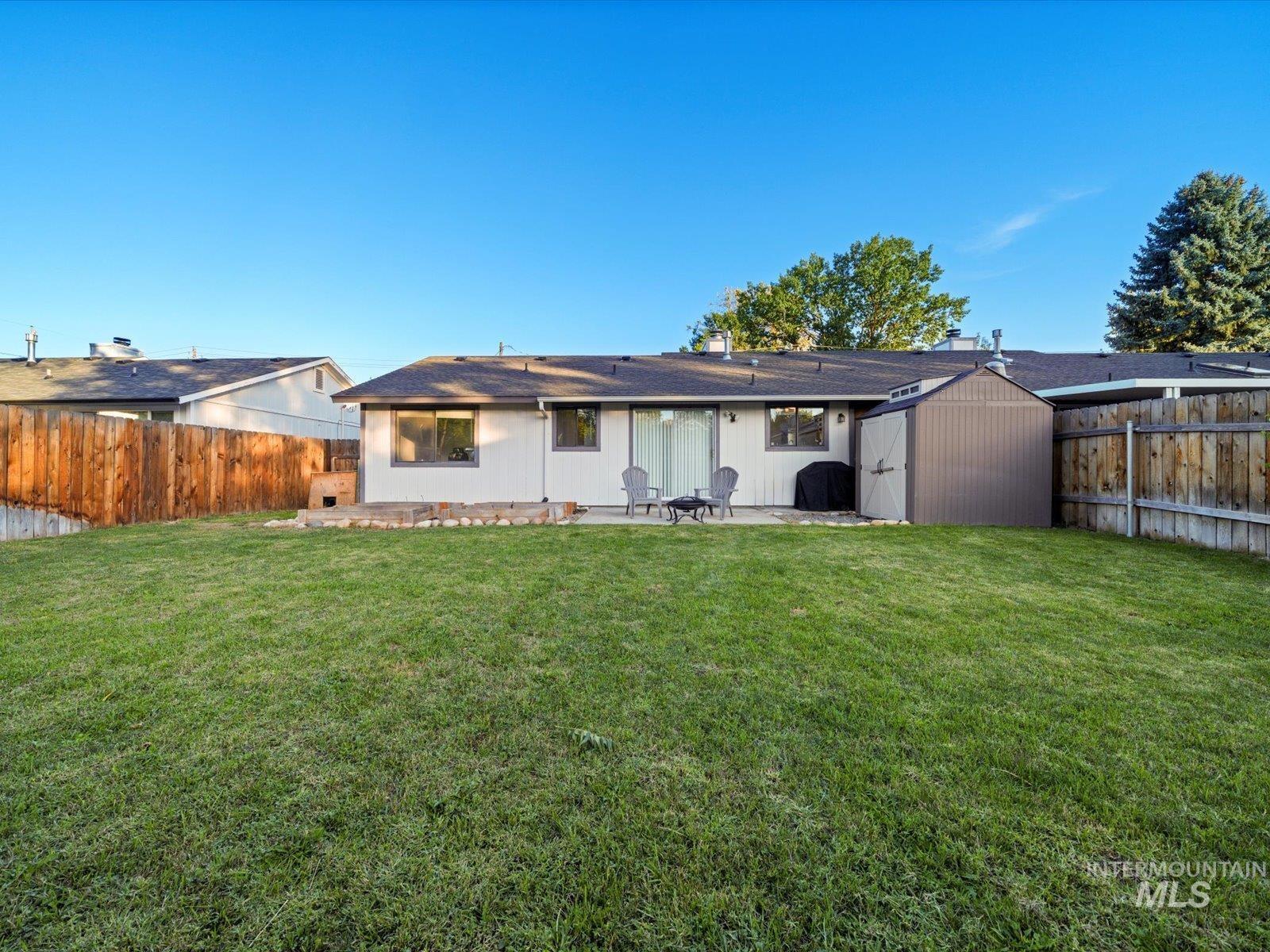 Back of house featuring a storage unit, a patio area, a fenced backyard, and a shingled roof