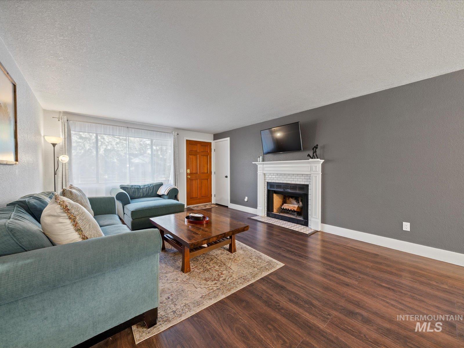 Living room featuring a fireplace, a textured ceiling, dark wood-style floors, and a textured wall