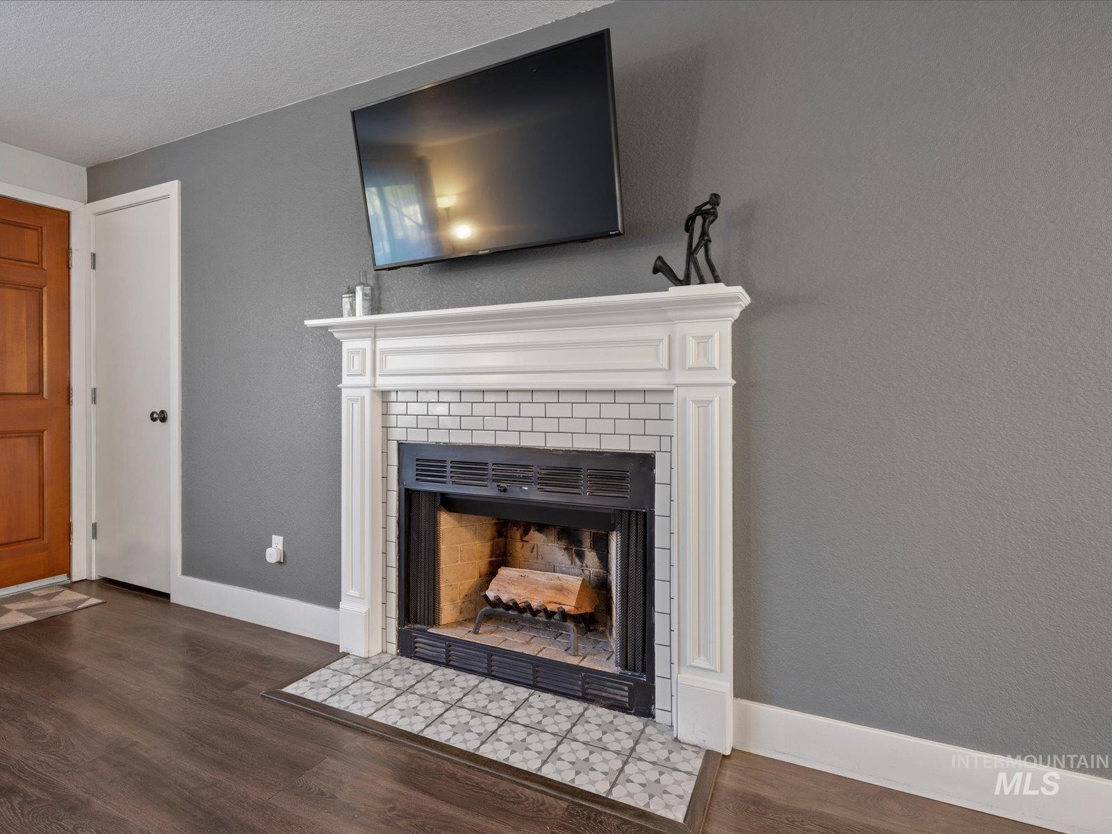 Detailed view of a fireplace, wood finished floors, a textured wall, and a textured ceiling