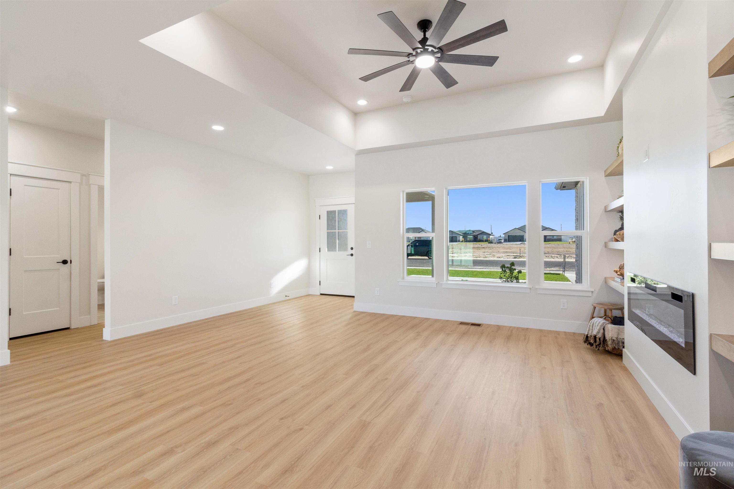 Unfurnished living room featuring light wood-type flooring, a tray ceiling, recessed lighting, and ceiling fan