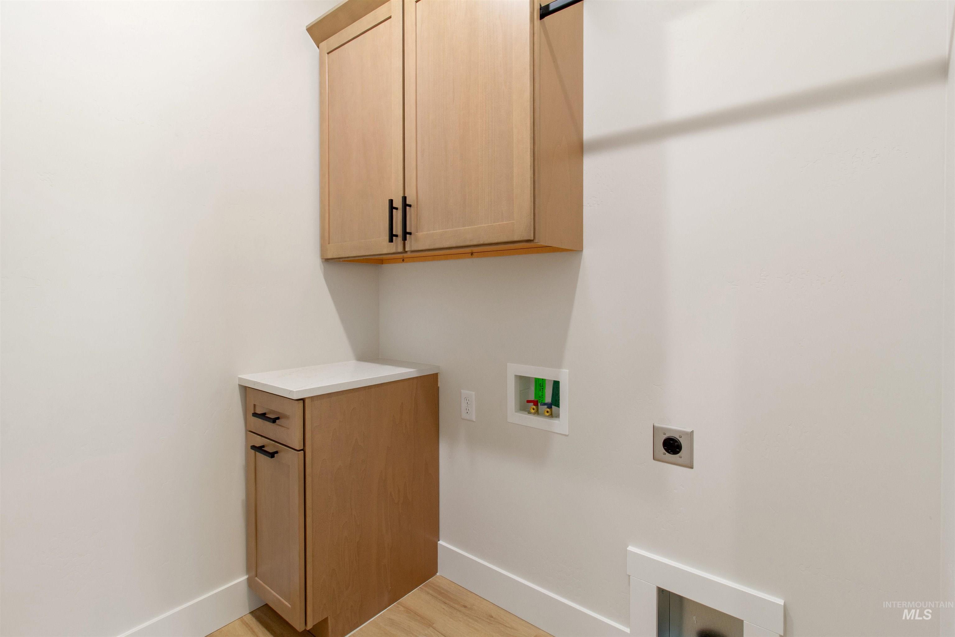 Laundry room with cabinet space, light wood finished floors, hookup for a washing machine, and electric dryer hookup