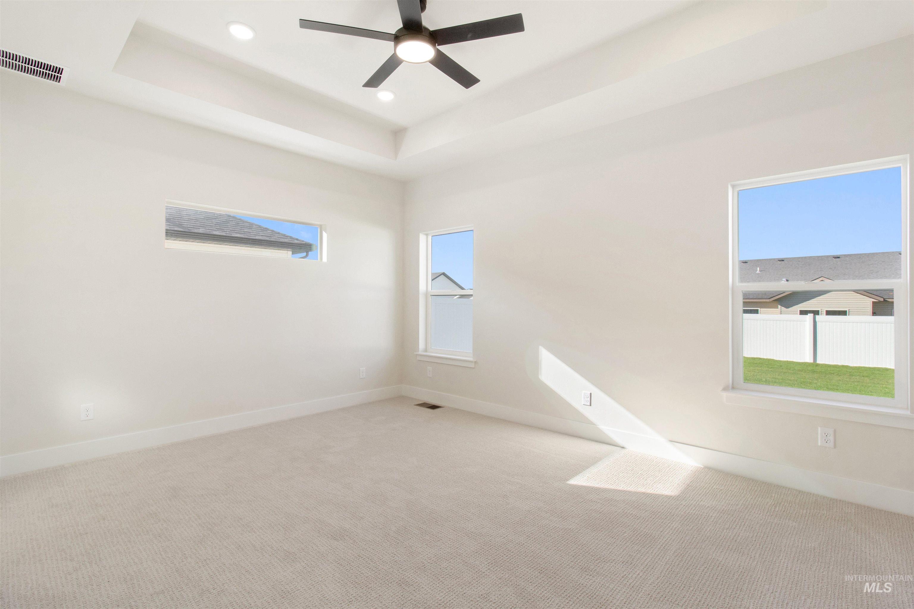 Carpeted spare room with a tray ceiling, healthy amount of natural light, ceiling fan, and recessed lighting