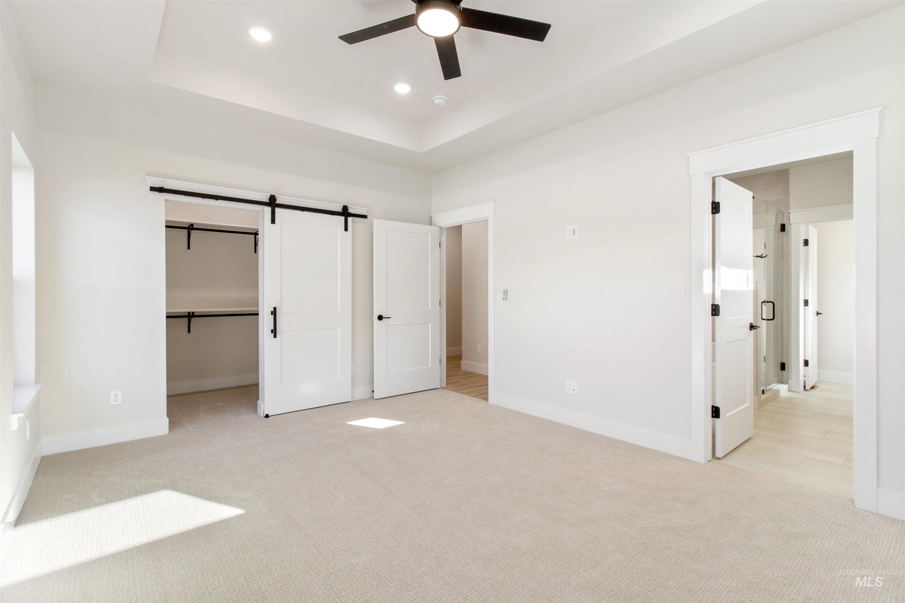 Unfurnished bedroom with a raised ceiling, carpet flooring, a barn door, recessed lighting, and ceiling fan
