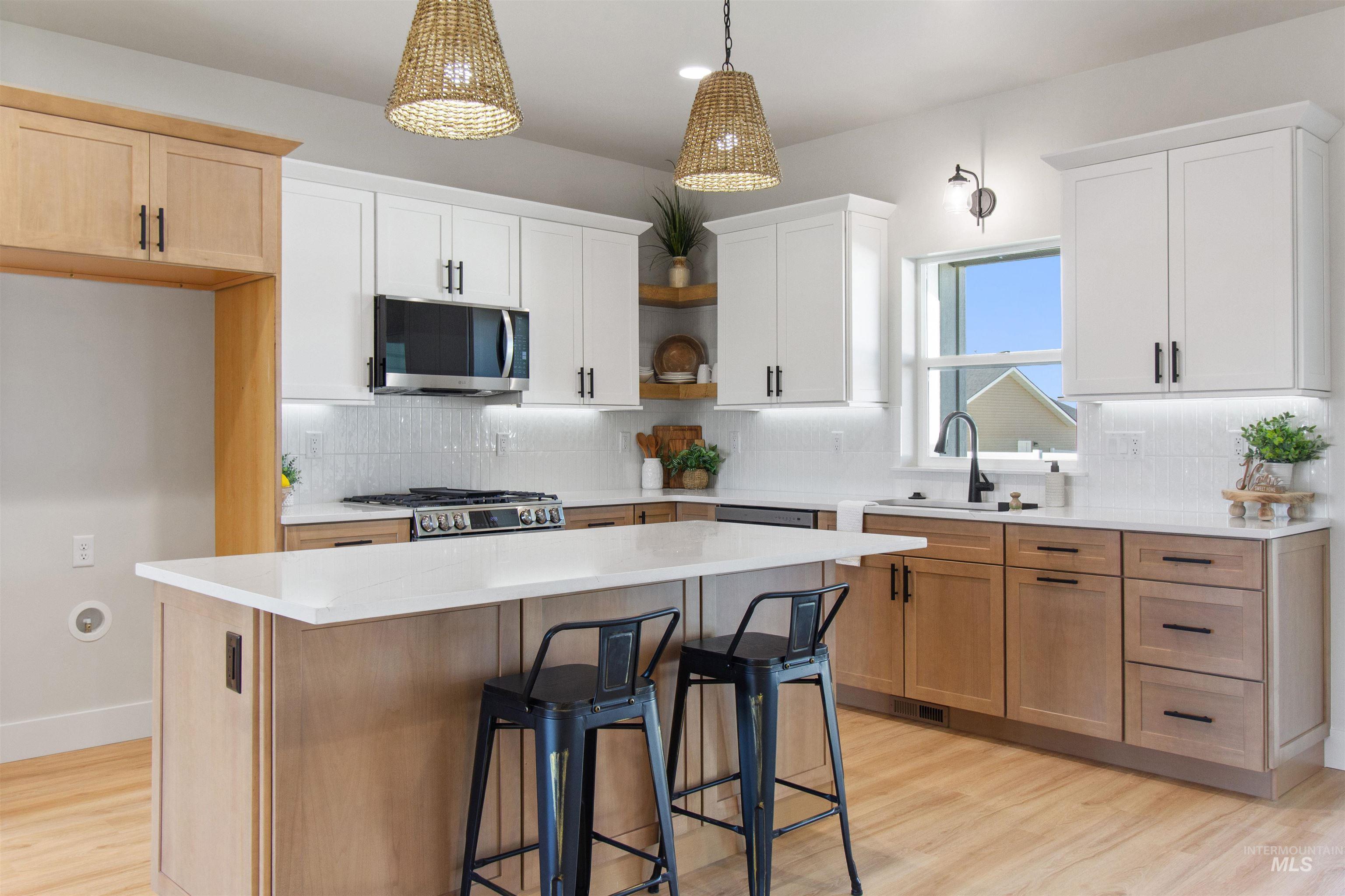Kitchen with decorative backsplash, a kitchen island, hanging light fixtures, appliances with stainless steel finishes, and a kitchen bar