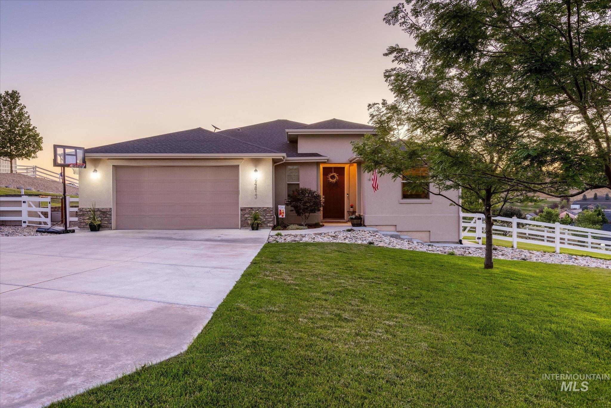View of front facade featuring an attached garage, concrete driveway, stucco siding, a shingled roof, and stone siding