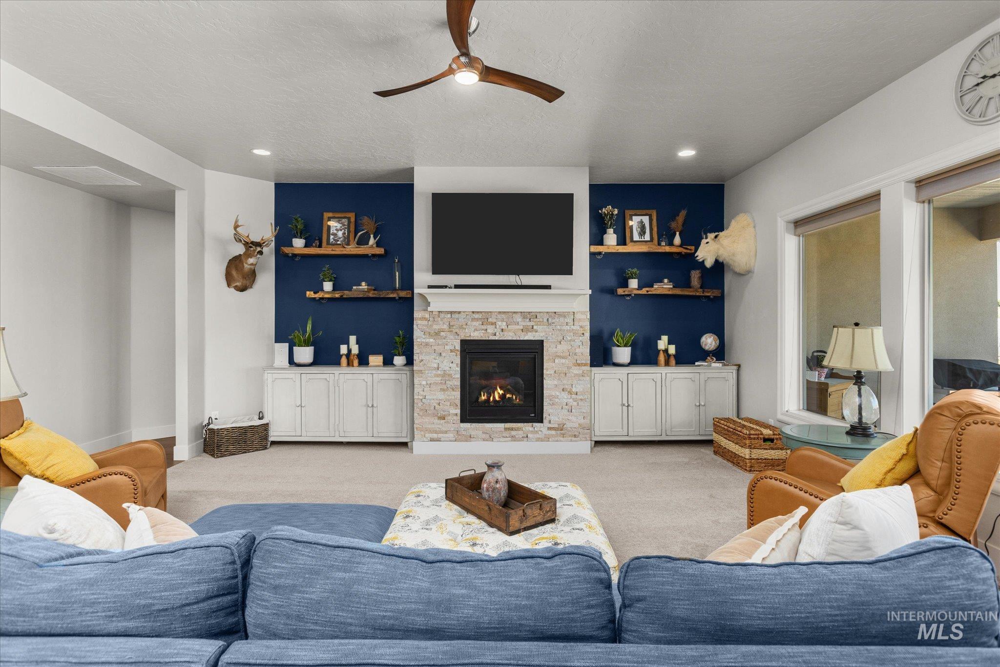 Carpeted living area with ceiling fan, a stone fireplace, recessed lighting, and a textured ceiling
