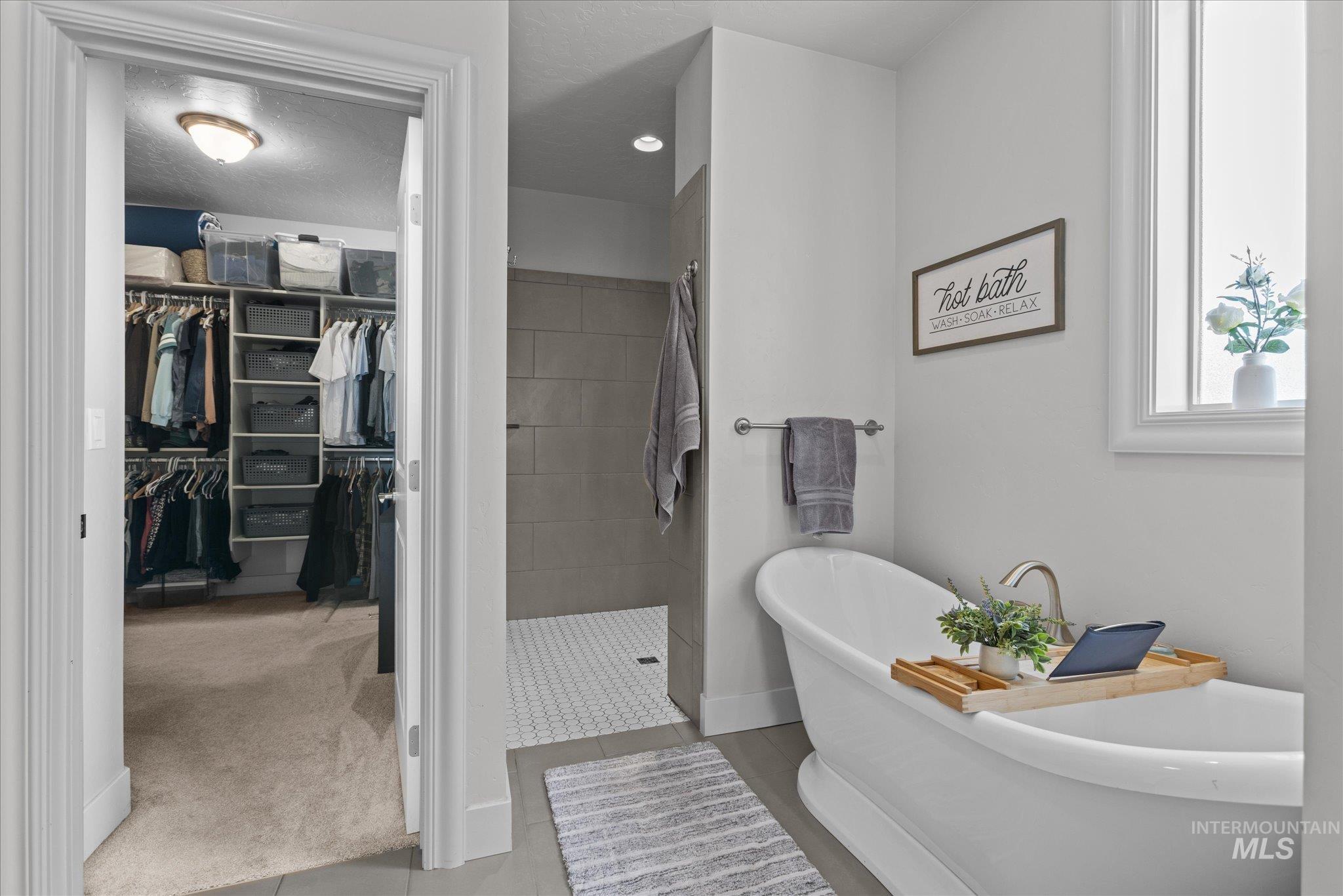 Bathroom with a freestanding tub, a spacious closet, tiled shower, and tile patterned flooring