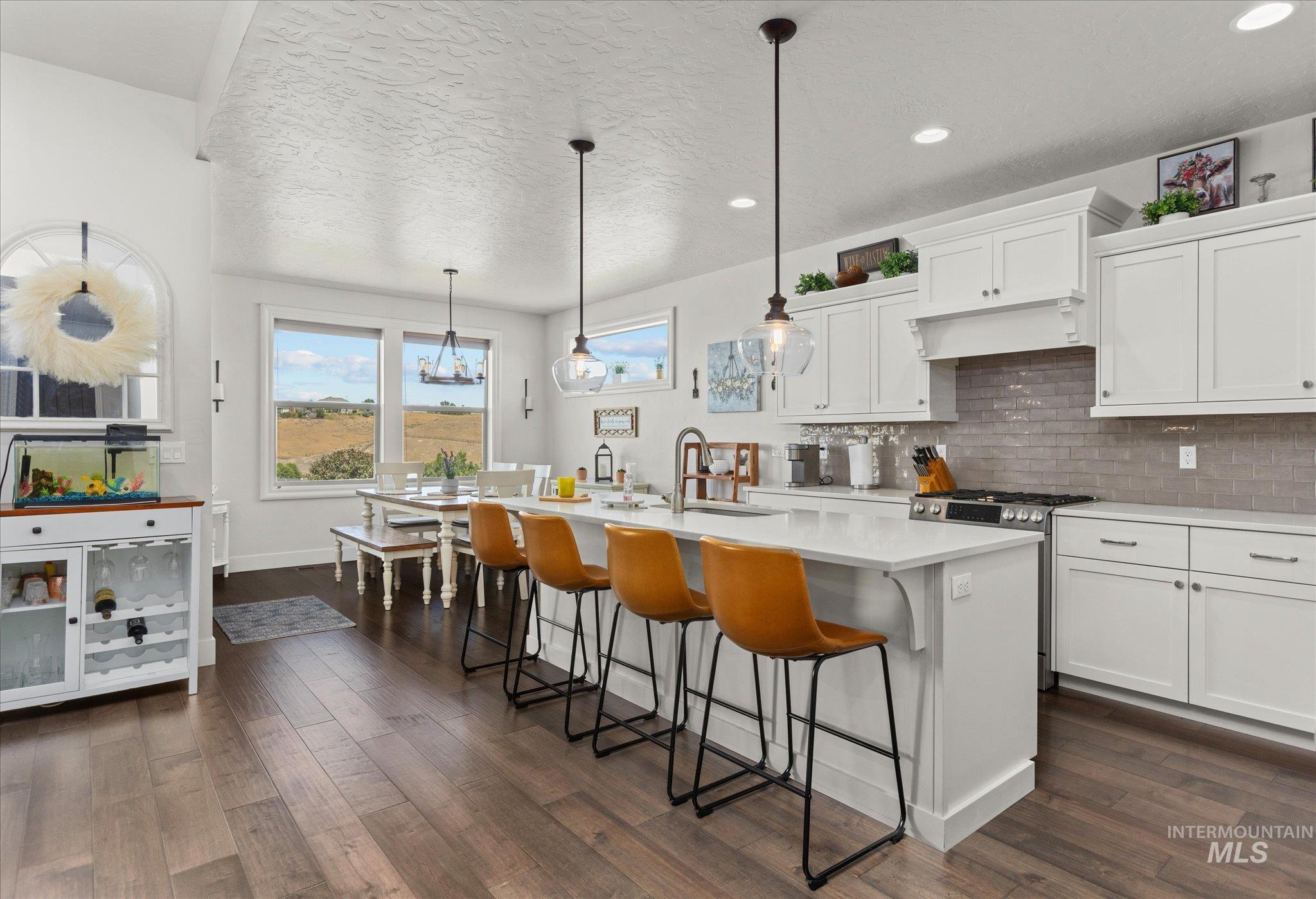 Kitchen with decorative backsplash, a textured ceiling, light countertops, a kitchen bar, and a kitchen island with sink