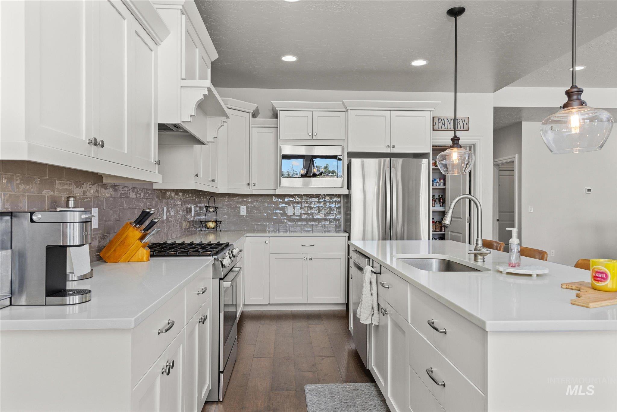 Kitchen with stainless steel appliances, decorative backsplash, a center island with sink, dark wood-type flooring, and light countertops