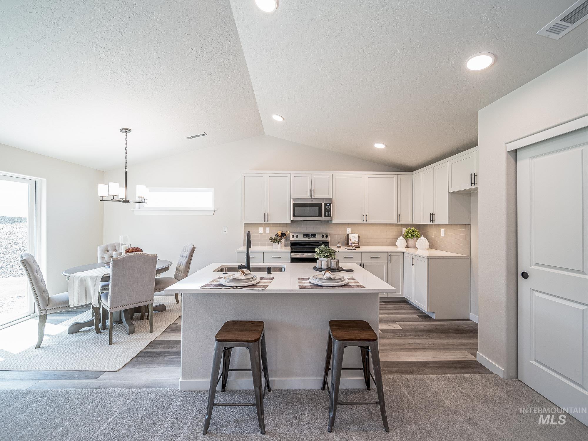 Kitchen featuring appliances with stainless steel finishes, vaulted ceiling, white cabinets, light countertops, and an island with sink
