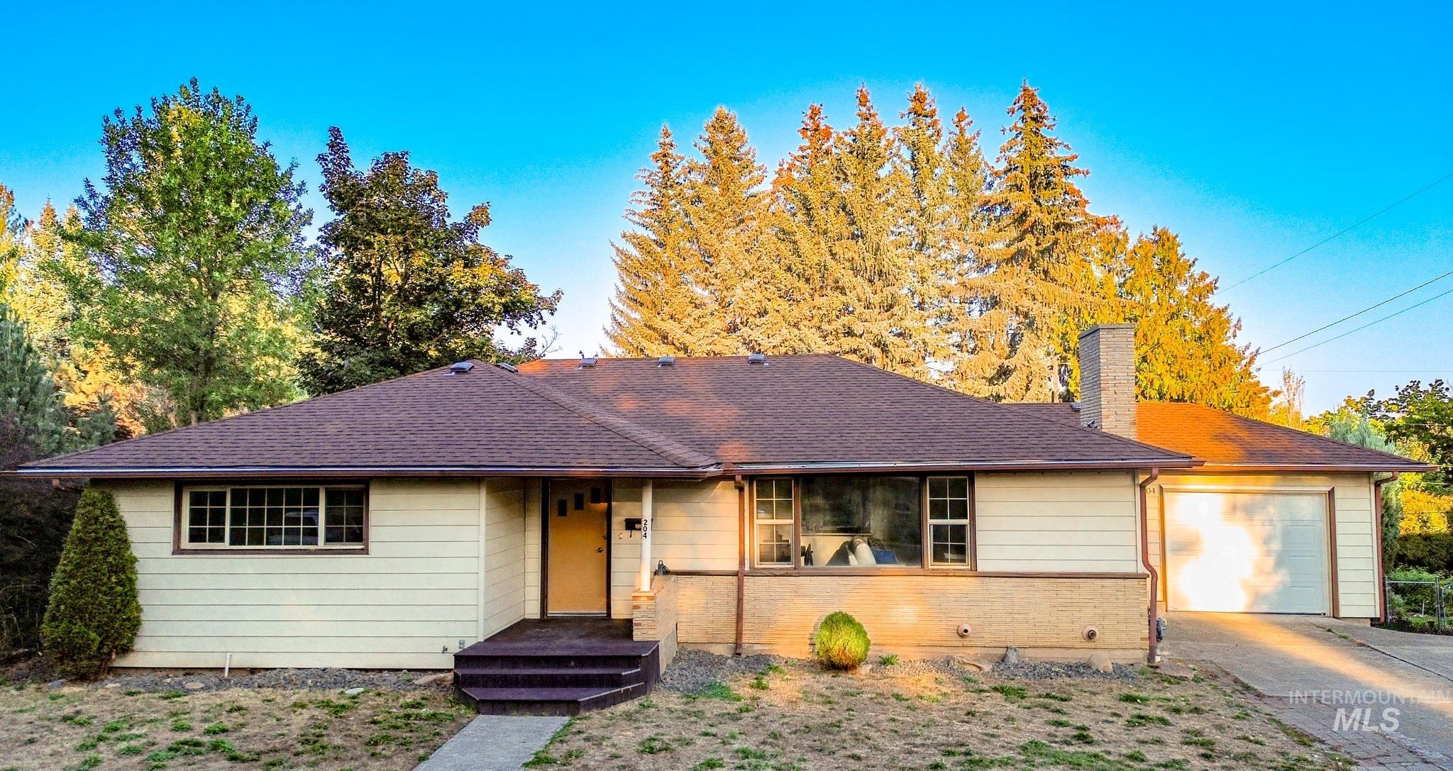 Single story home with a chimney, driveway, brick siding, a shingled roof, and a garage