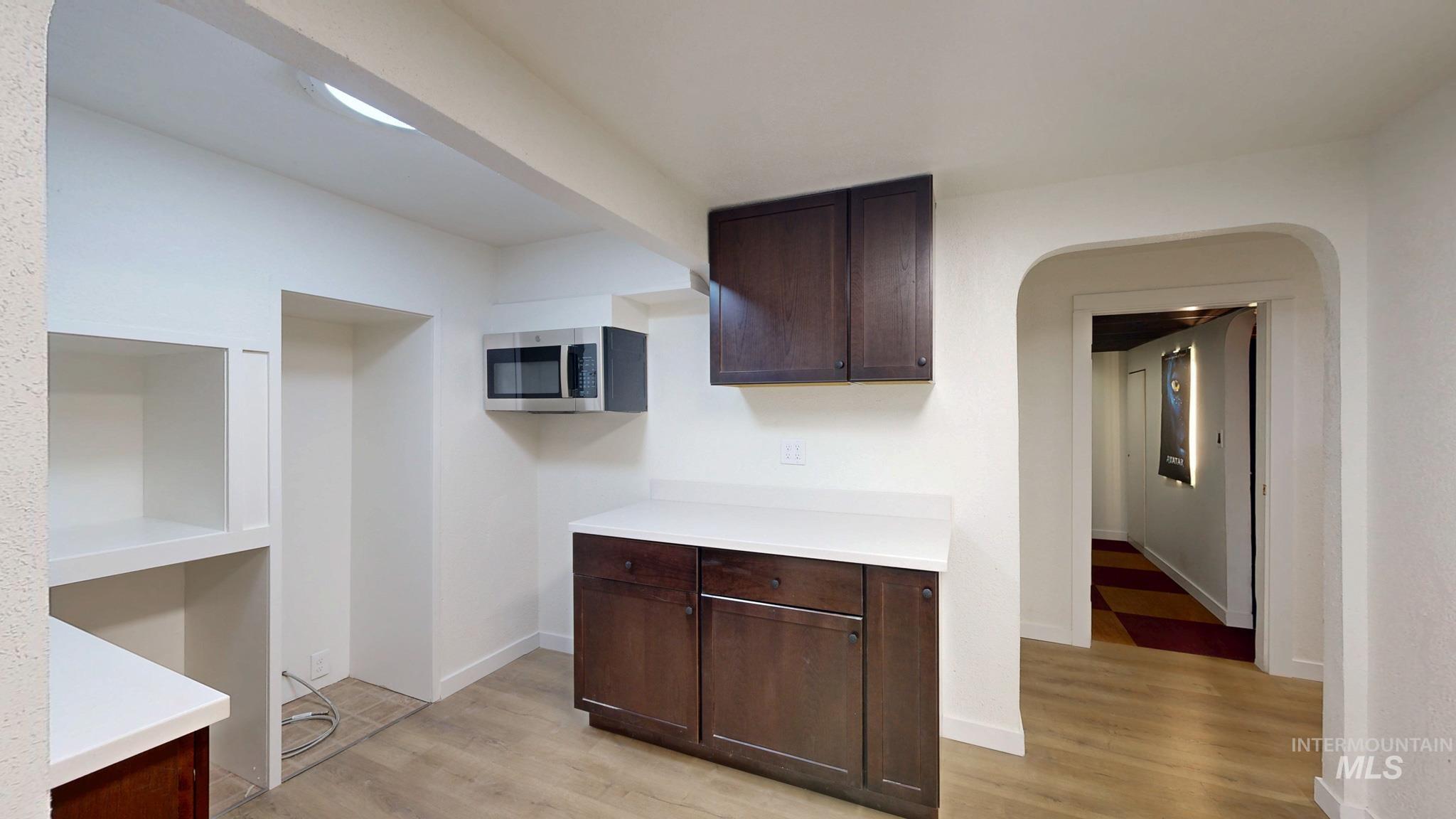 Kitchen with dark brown cabinetry, arched walkways, light wood finished floors, and stainless steel microwave