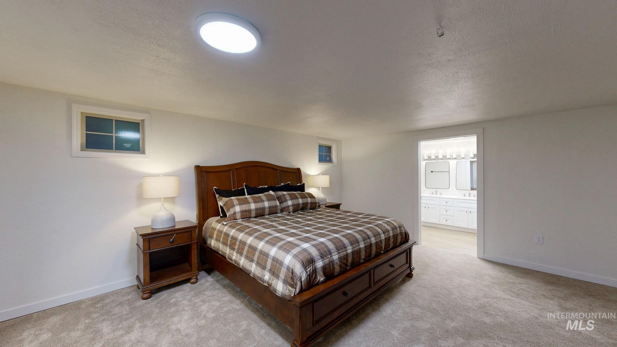 Bedroom with a textured ceiling, light carpet, and ensuite bath