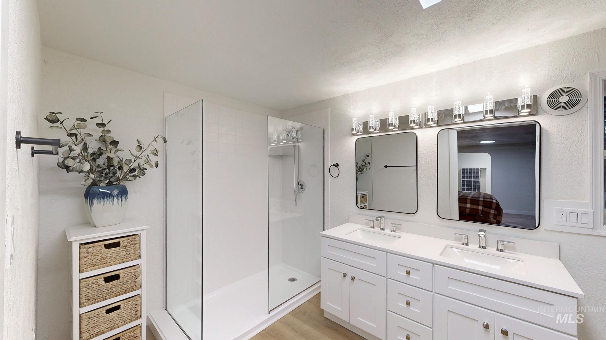 Bathroom with a stall shower, double vanity, light wood-style floors, and a textured wall
