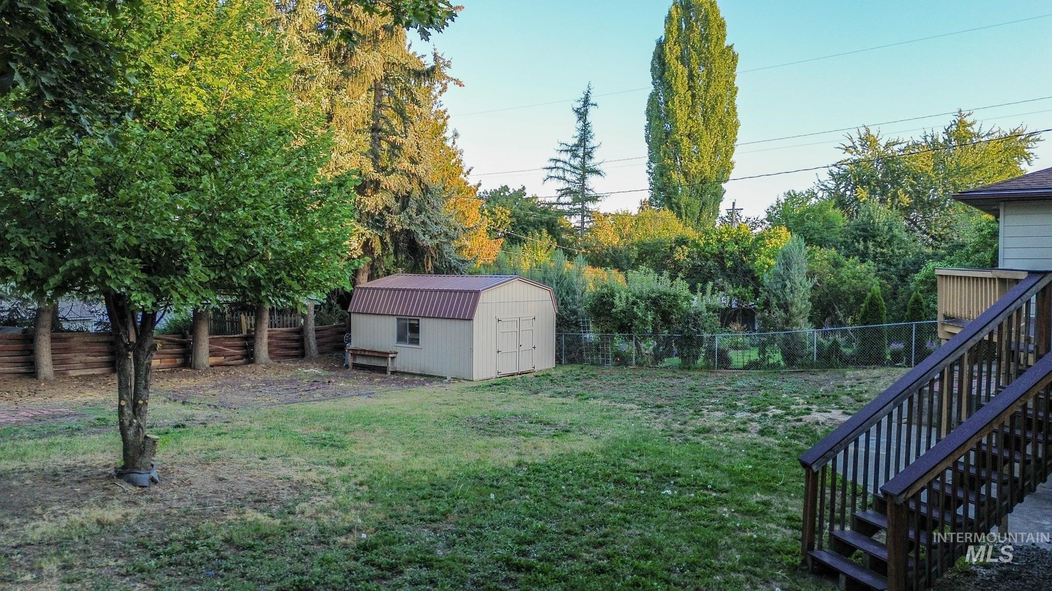 Fenced backyard featuring a storage unit and view of scattered trees