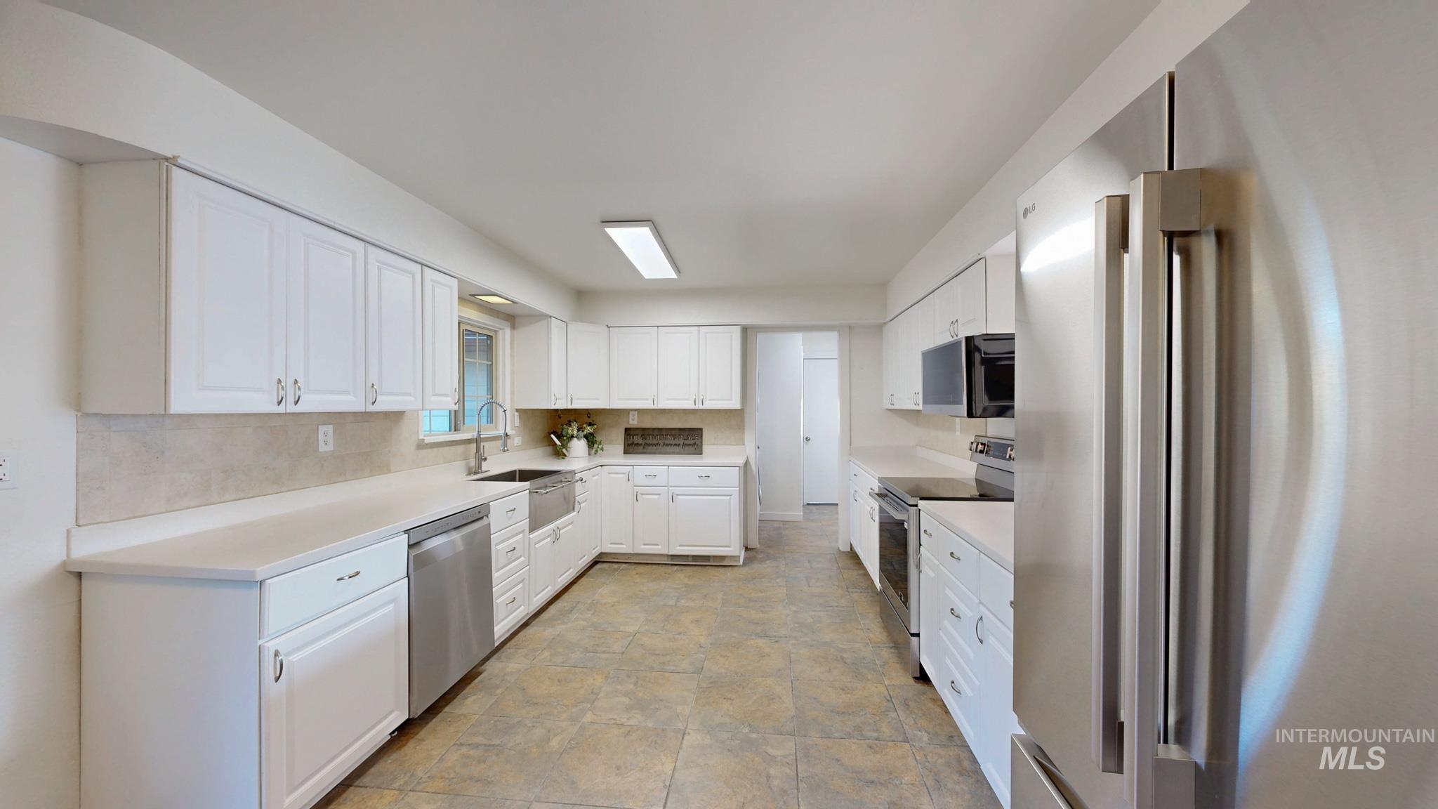 Kitchen with appliances with stainless steel finishes, light countertops, white cabinets, and tasteful backsplash