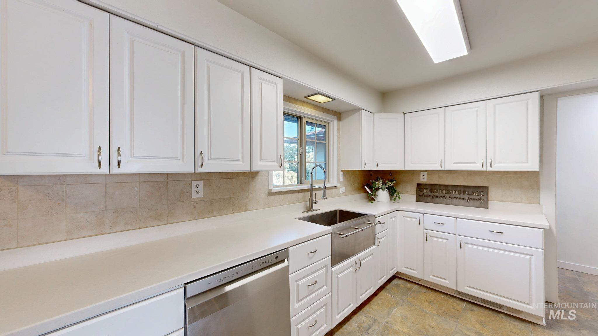 Kitchen featuring dishwasher, white cabinetry, backsplash, and light stone finish floors