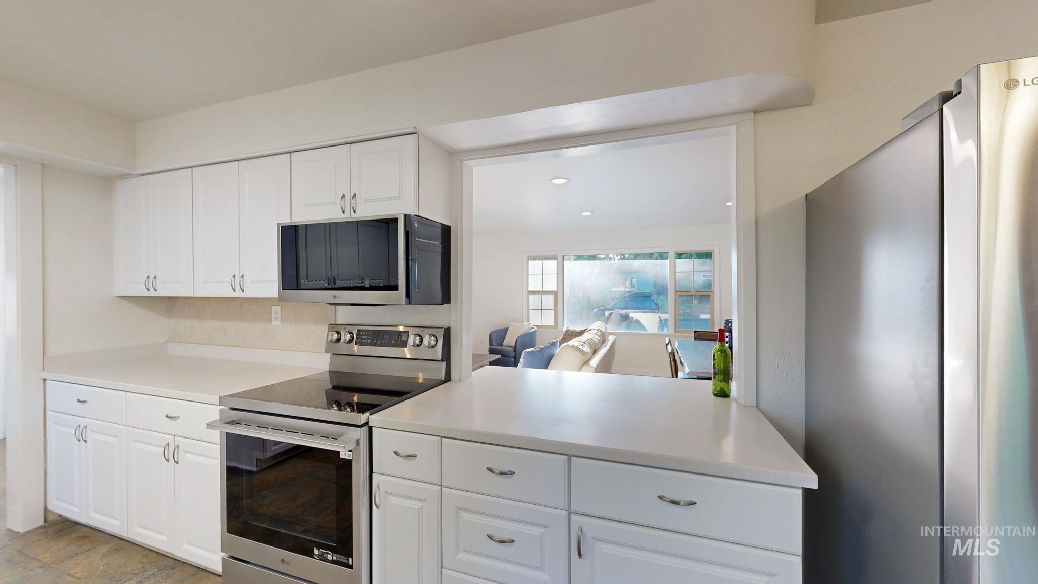 Kitchen featuring stainless steel appliances, light countertops, white cabinets, recessed lighting, and open floor plan