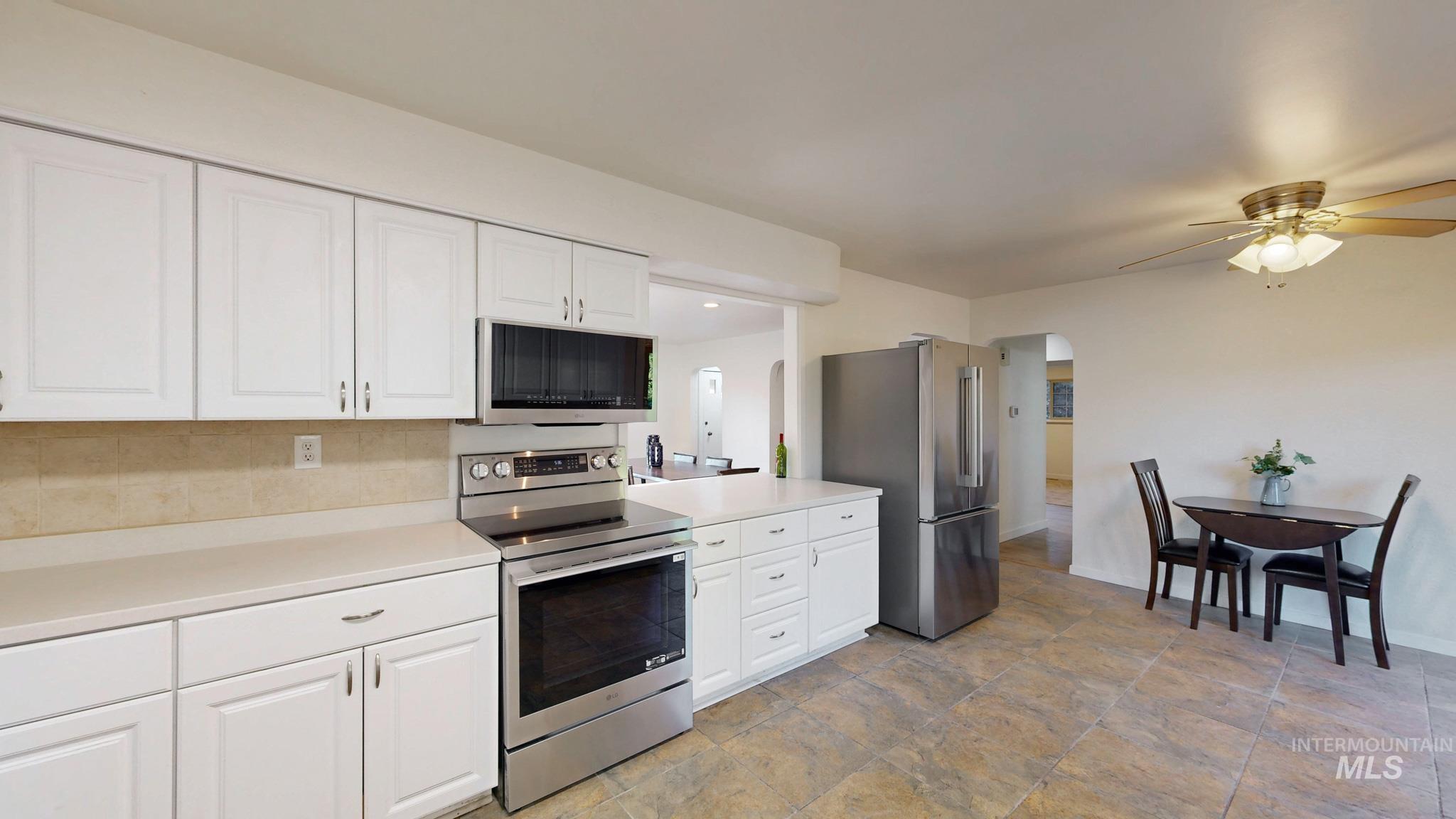 Kitchen with stainless steel appliances, arched walkways, white cabinets, light countertops, and ceiling fan