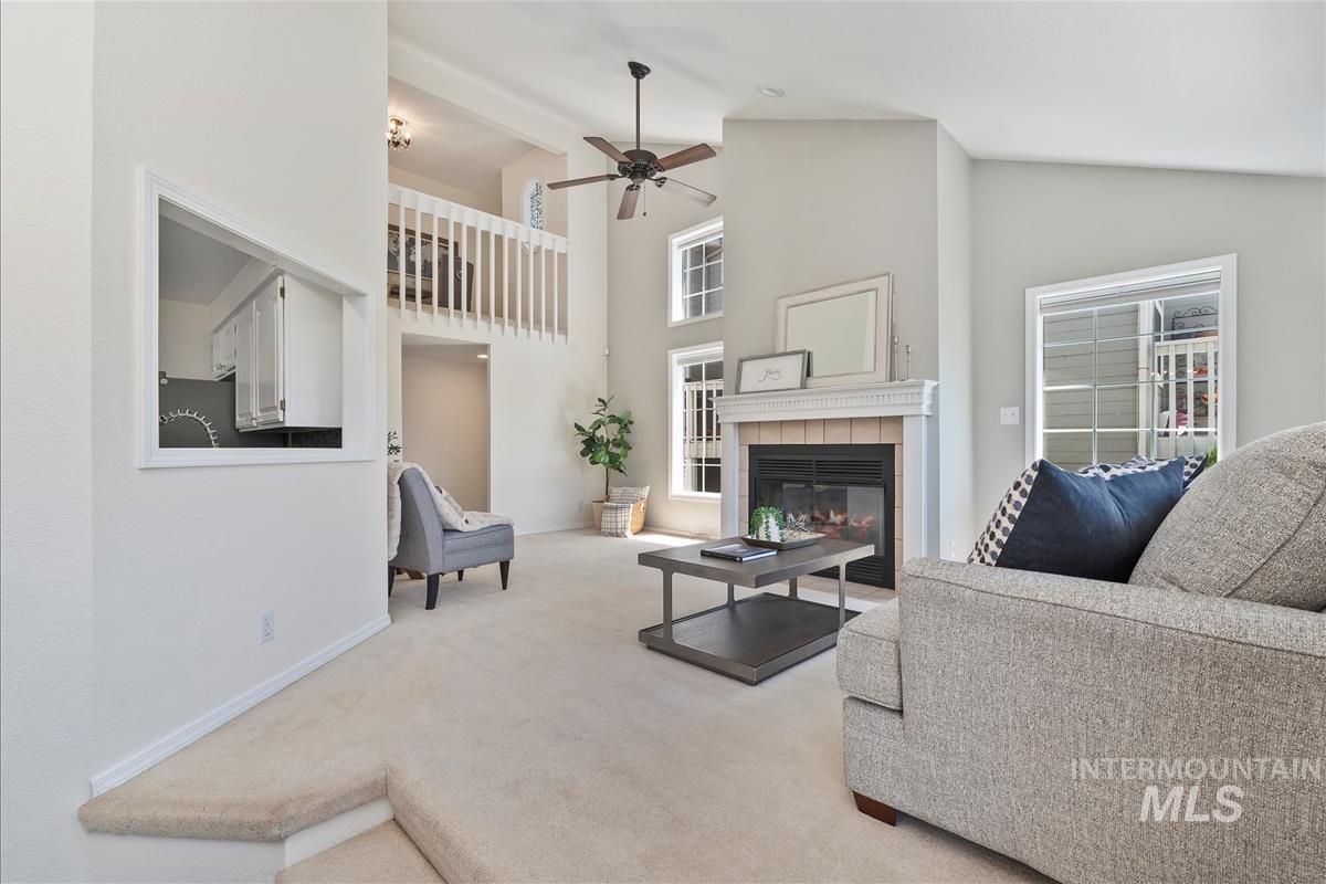 Living area featuring ceiling fan, a fireplace, carpet flooring, and high vaulted ceiling