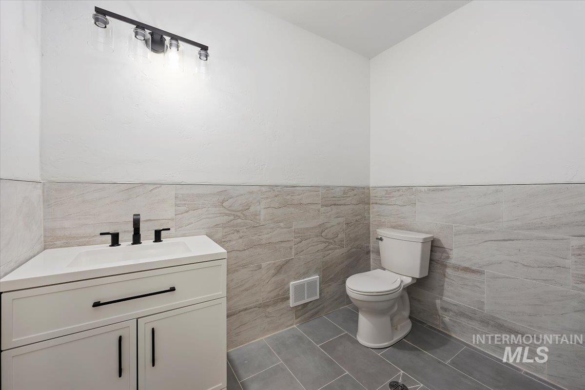 Half bath with vanity, tile walls, tile patterned flooring, and wainscoting