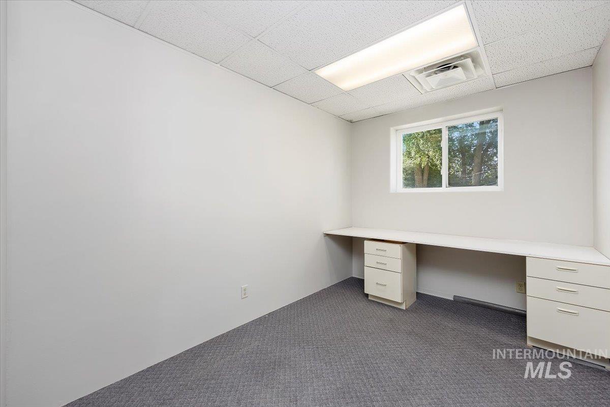 Unfurnished office featuring dark carpet, a drop ceiling, and built in desk