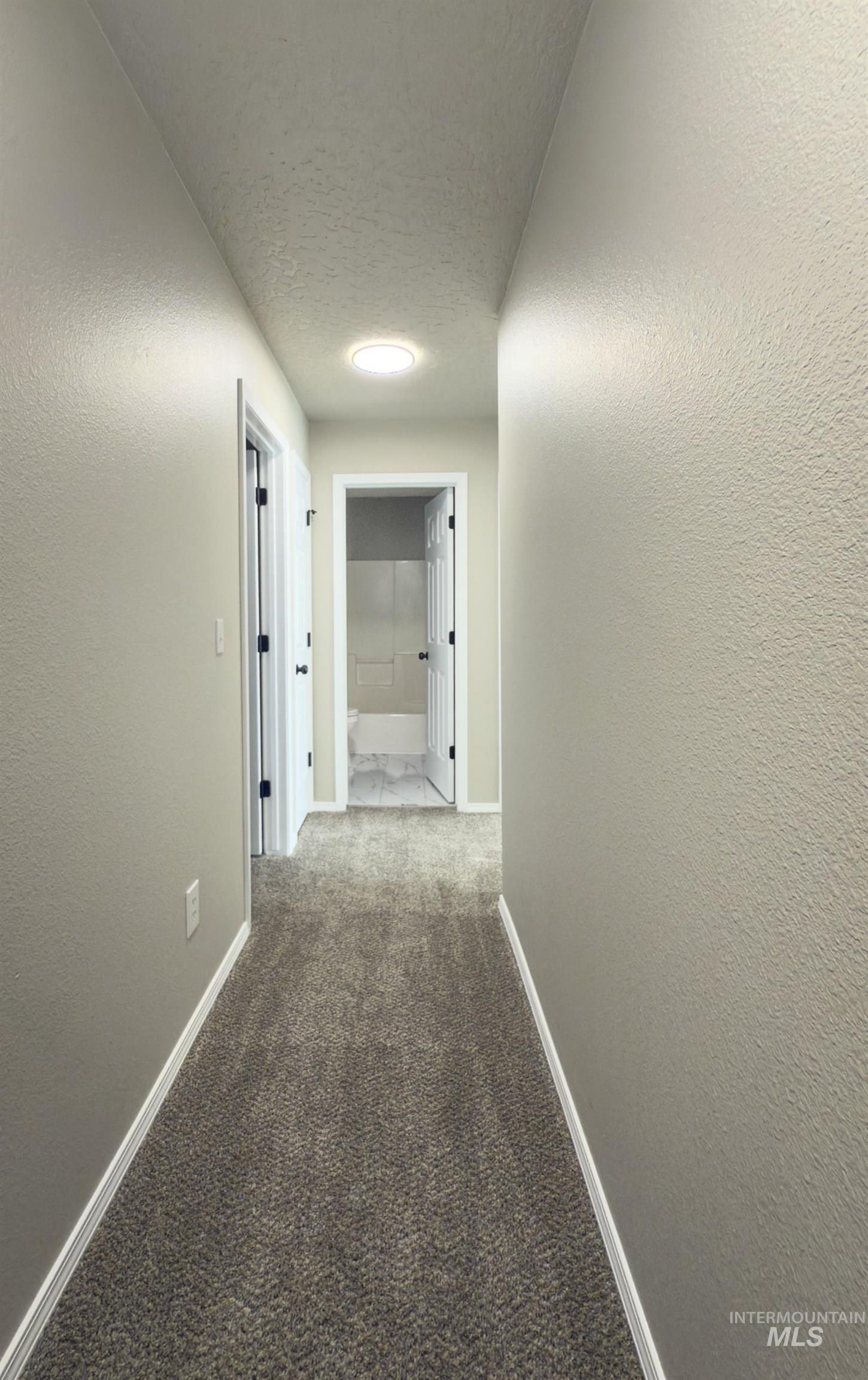 Hall with carpet flooring, a textured wall, and a textured ceiling