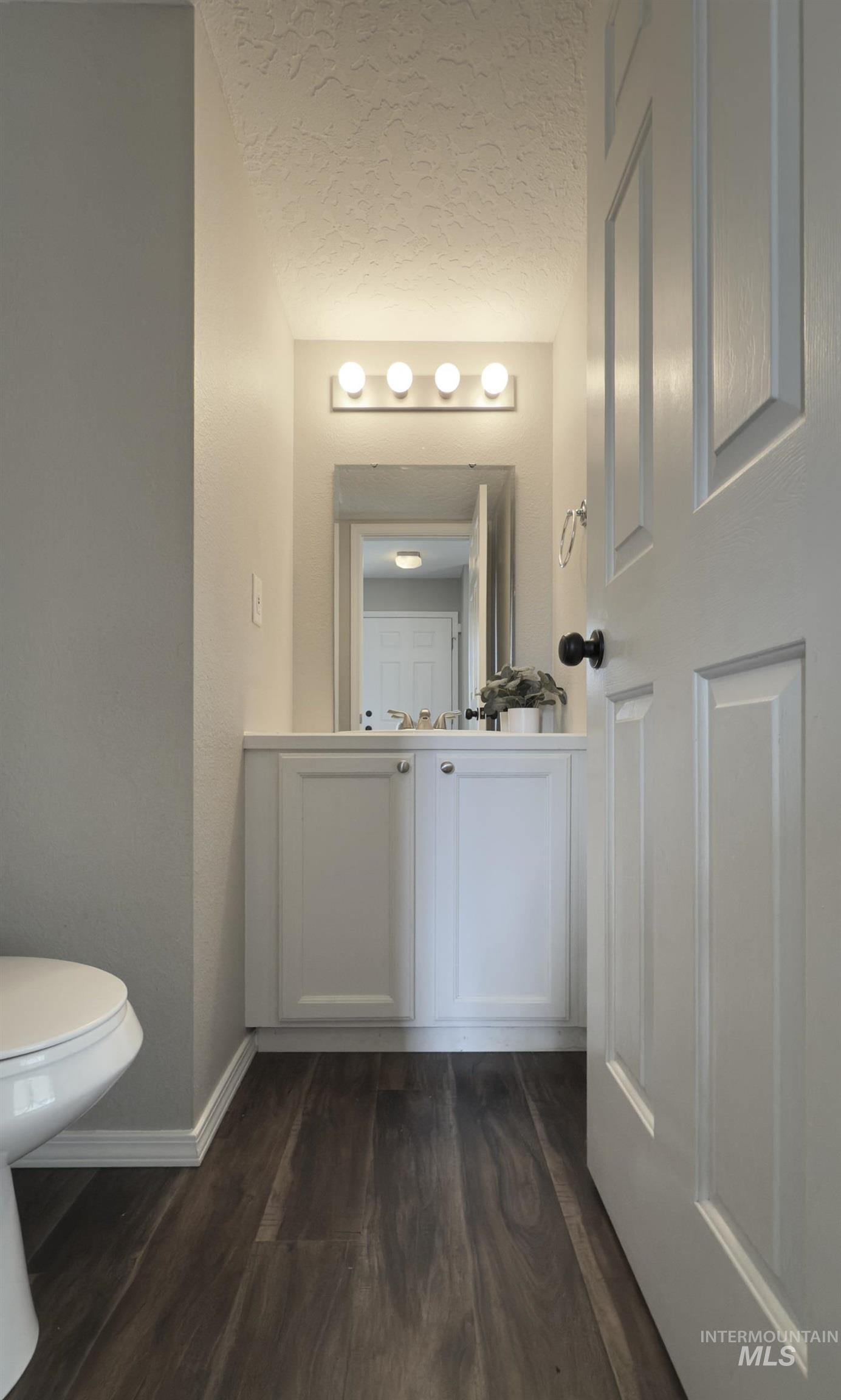 Half bathroom featuring vanity, dark wood-type flooring, and a textured ceiling
