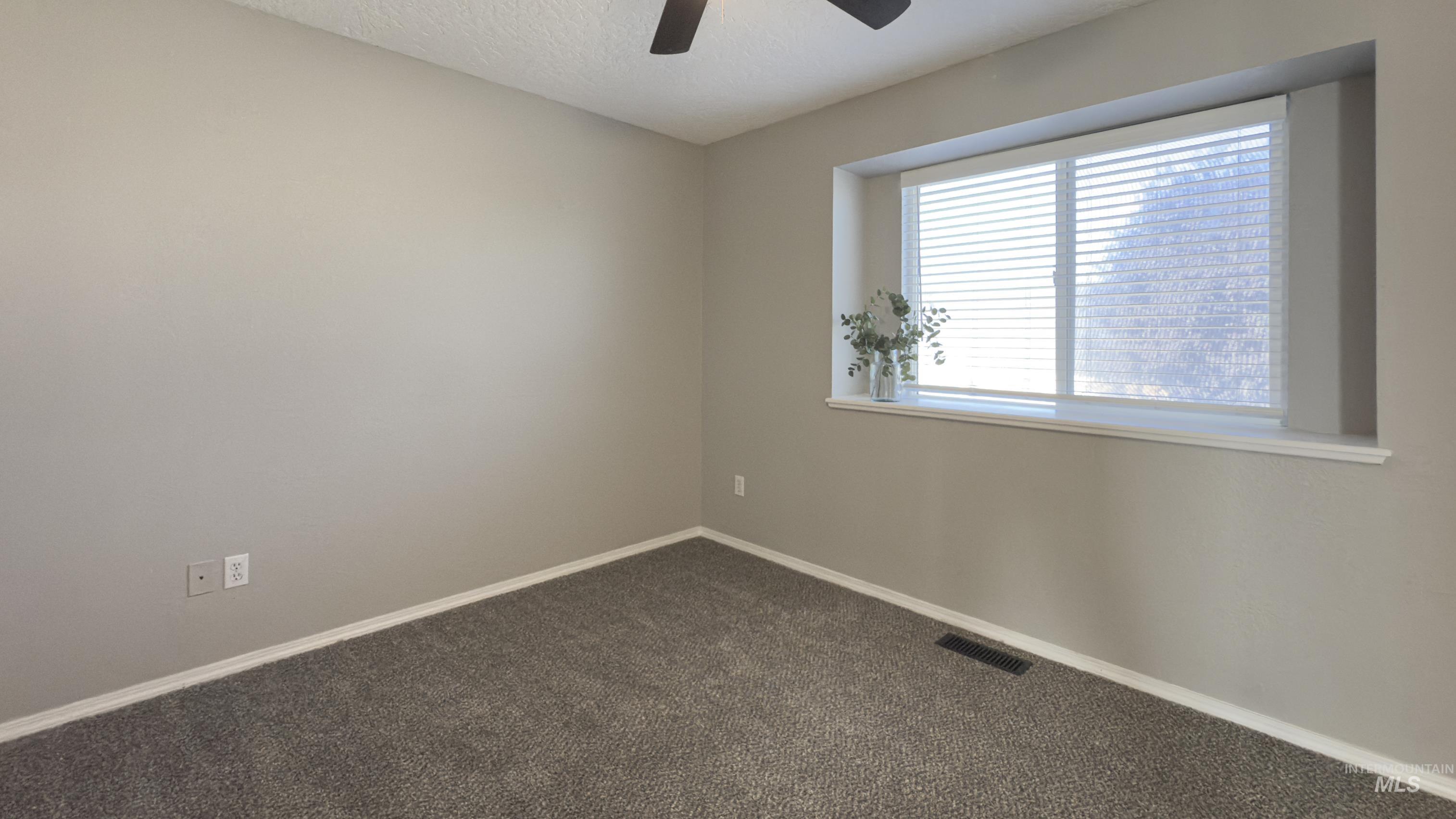 Empty room featuring dark carpet, a textured ceiling, and a ceiling fan