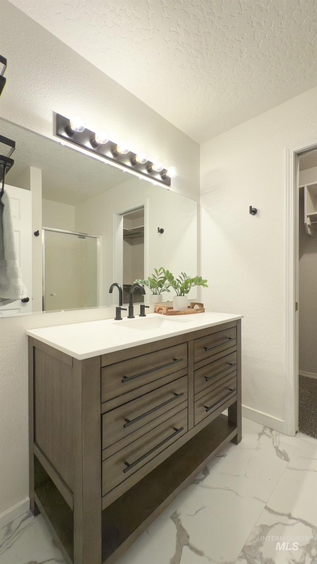 Bathroom featuring light marble finish flooring, vanity, a shower stall, and a textured ceiling