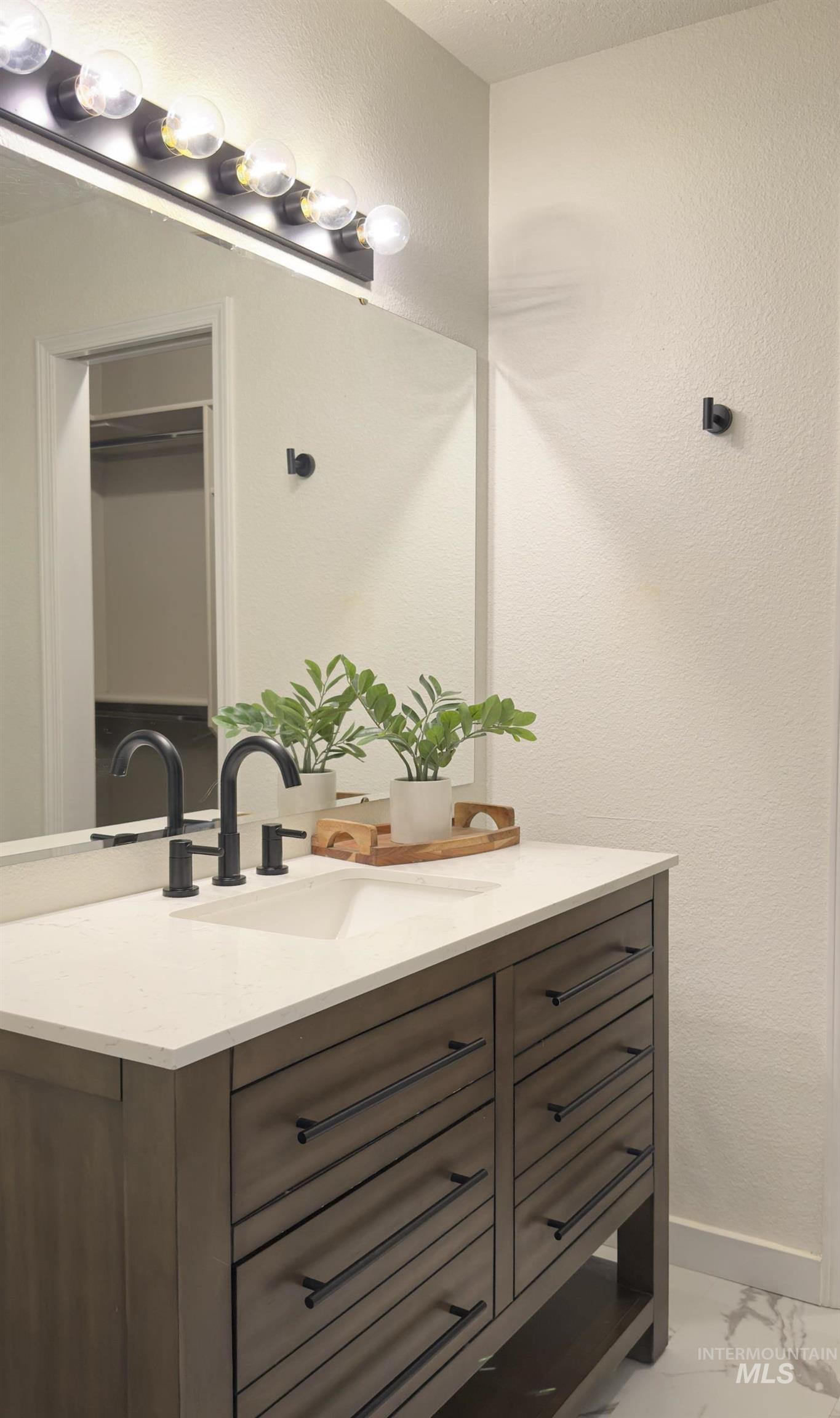 Bathroom with a textured wall, vanity, light marble finish flooring, and a closet