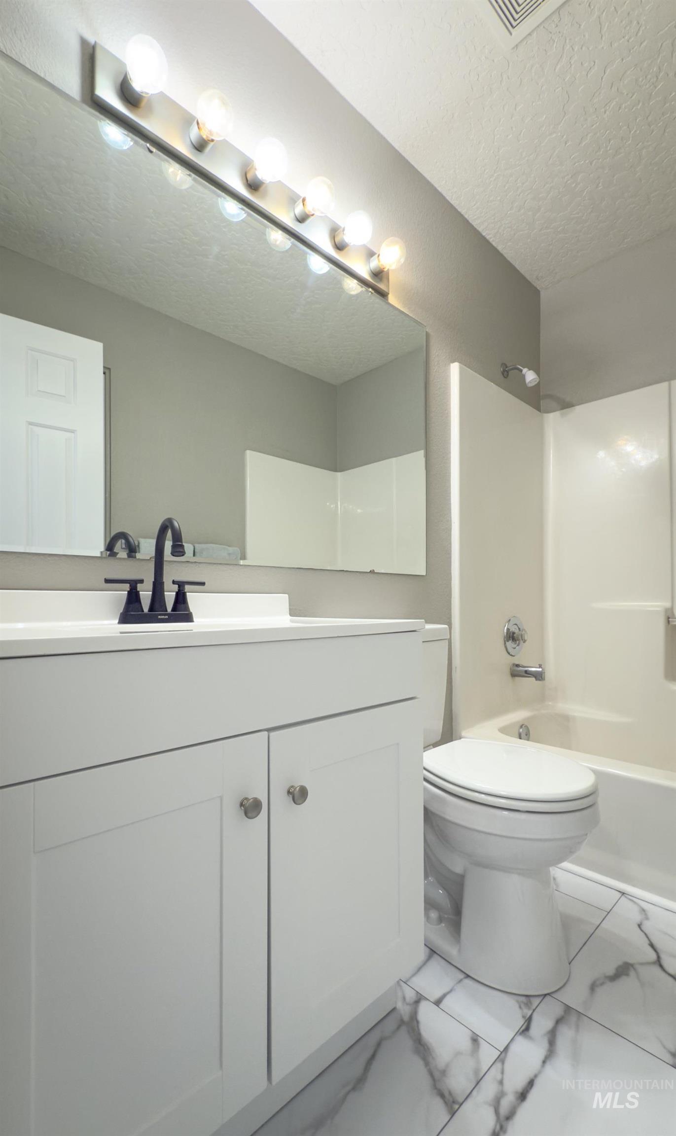Full bath featuring shower / tub combination, vanity, a textured ceiling, and marble finish flooring