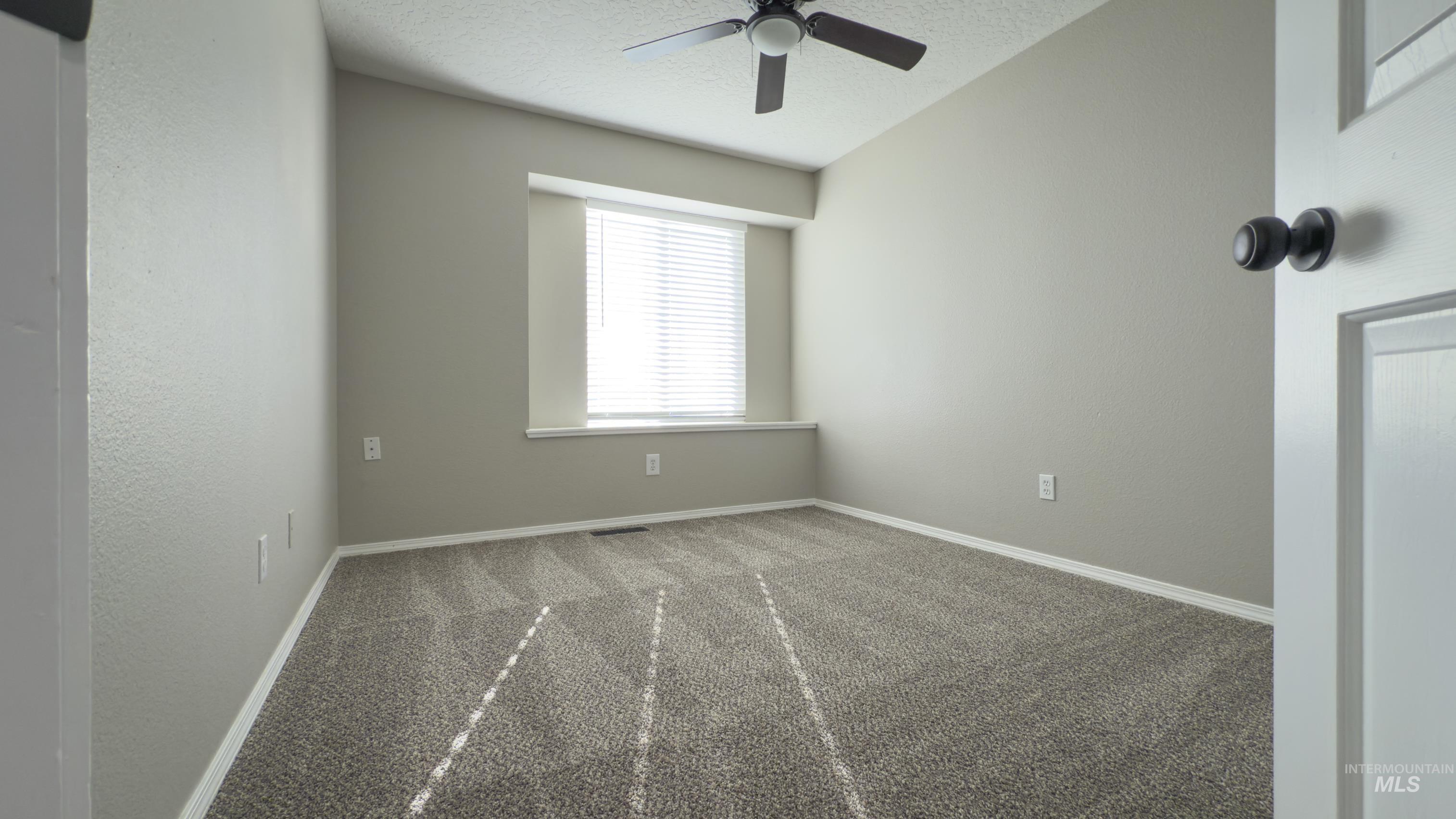 Carpeted empty room with a textured ceiling and ceiling fan
