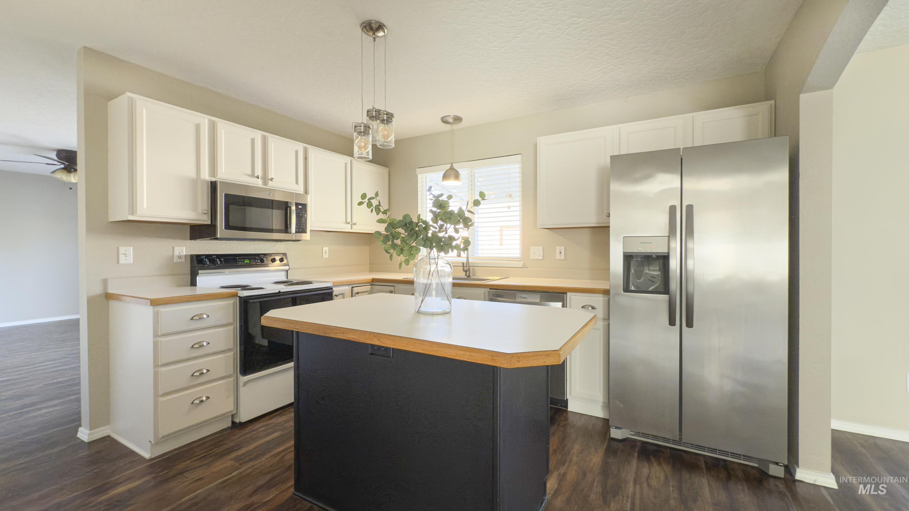 Kitchen with light countertops, stainless steel appliances, a center island, decorative light fixtures, and a textured ceiling